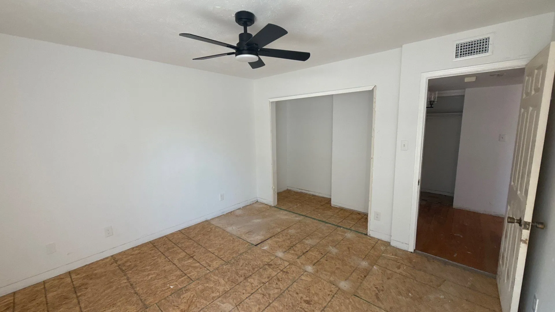Interior room with light-toned walls, ceiling-mounted fan, and exposed subflooring