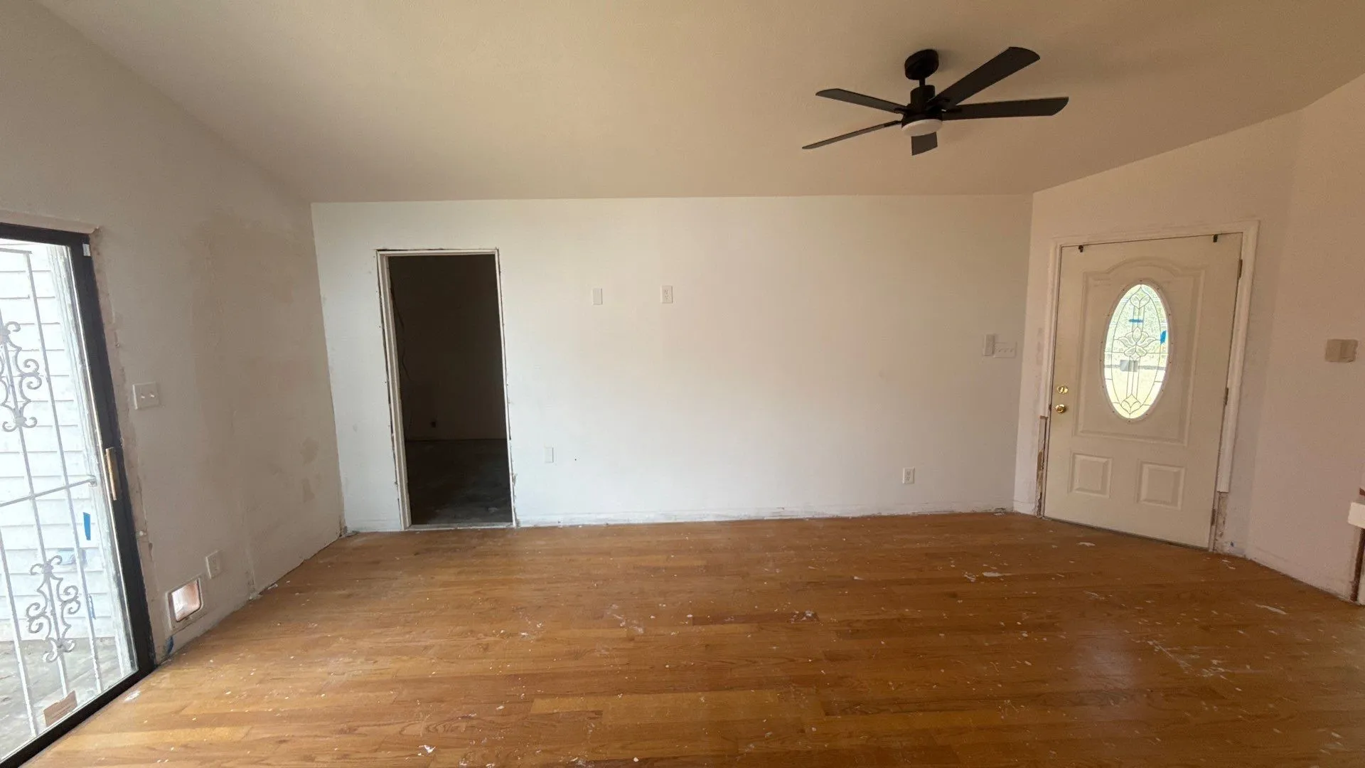 Hardwood-finish flooring, white walls, black ceiling fan, white entry door with decorative glass insert, and a sliding glass door