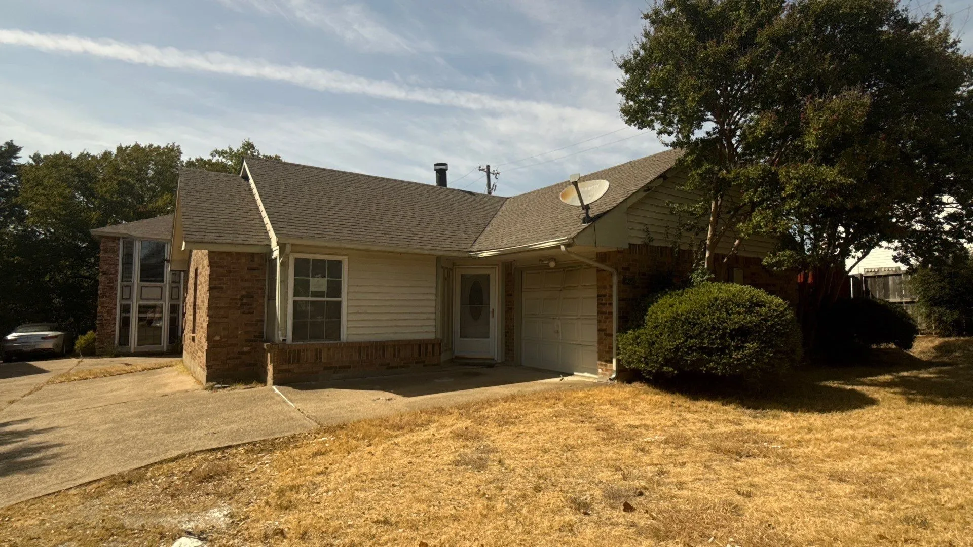Brick and siding exterior with an attached garage, featuring a shingle roof and mature trees