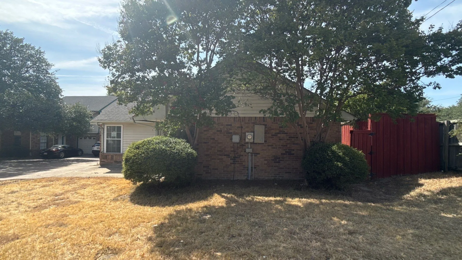 Brick exterior featuring siding accents, mature trees, and a red privacy fence