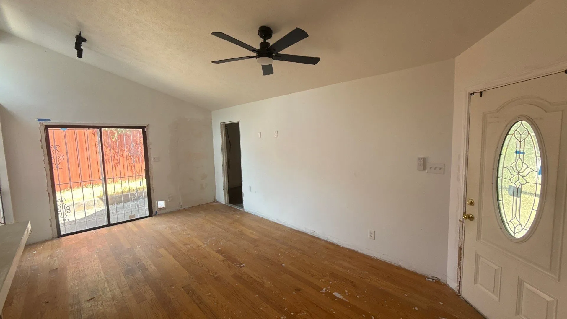 Vaulted ceiling with a ceiling fan, wood-finish flooring, sliding glass door, and an entryway door with decorative glass