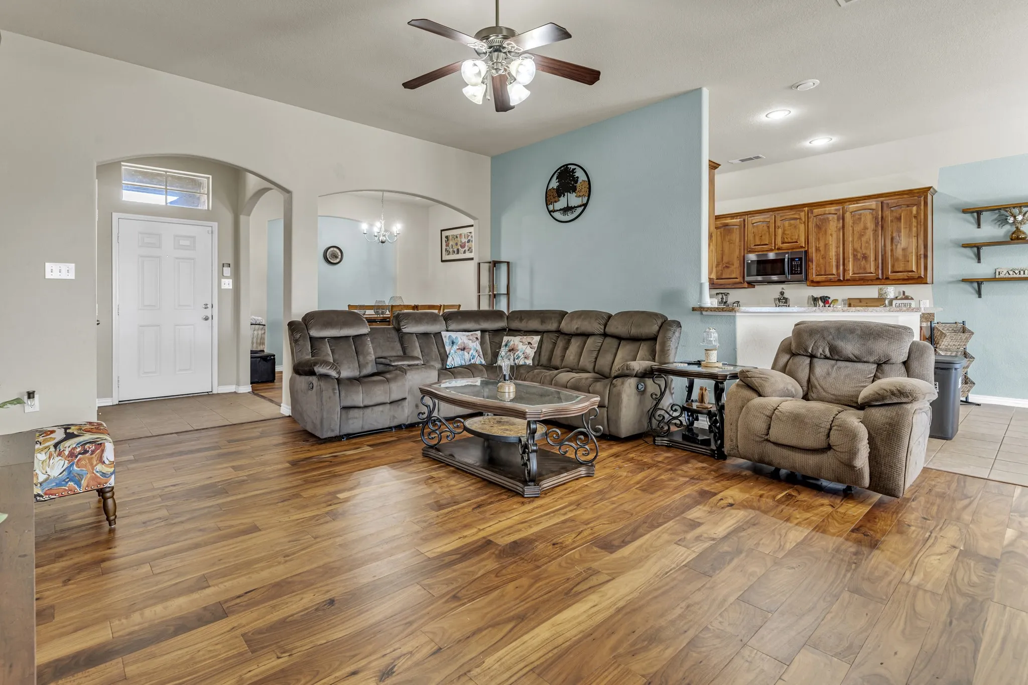 Wood-finish flooring throughout, ceiling fan with integrated lighting, arched doorways, and kitchen pass-through with wood cabinetry