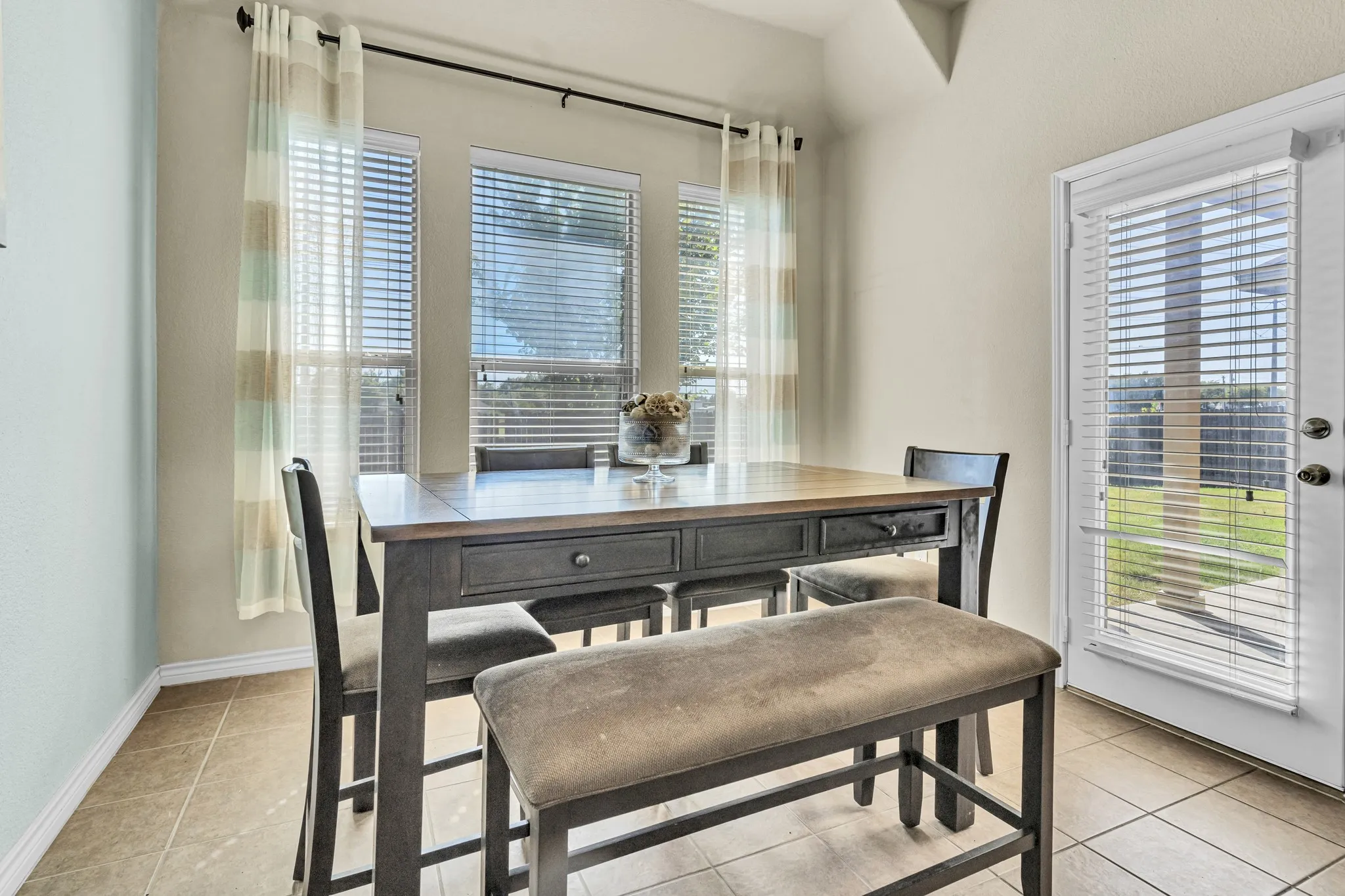 Multiple windows with horizontal blinds, tiled flooring, and a white exterior door with integrated blinds