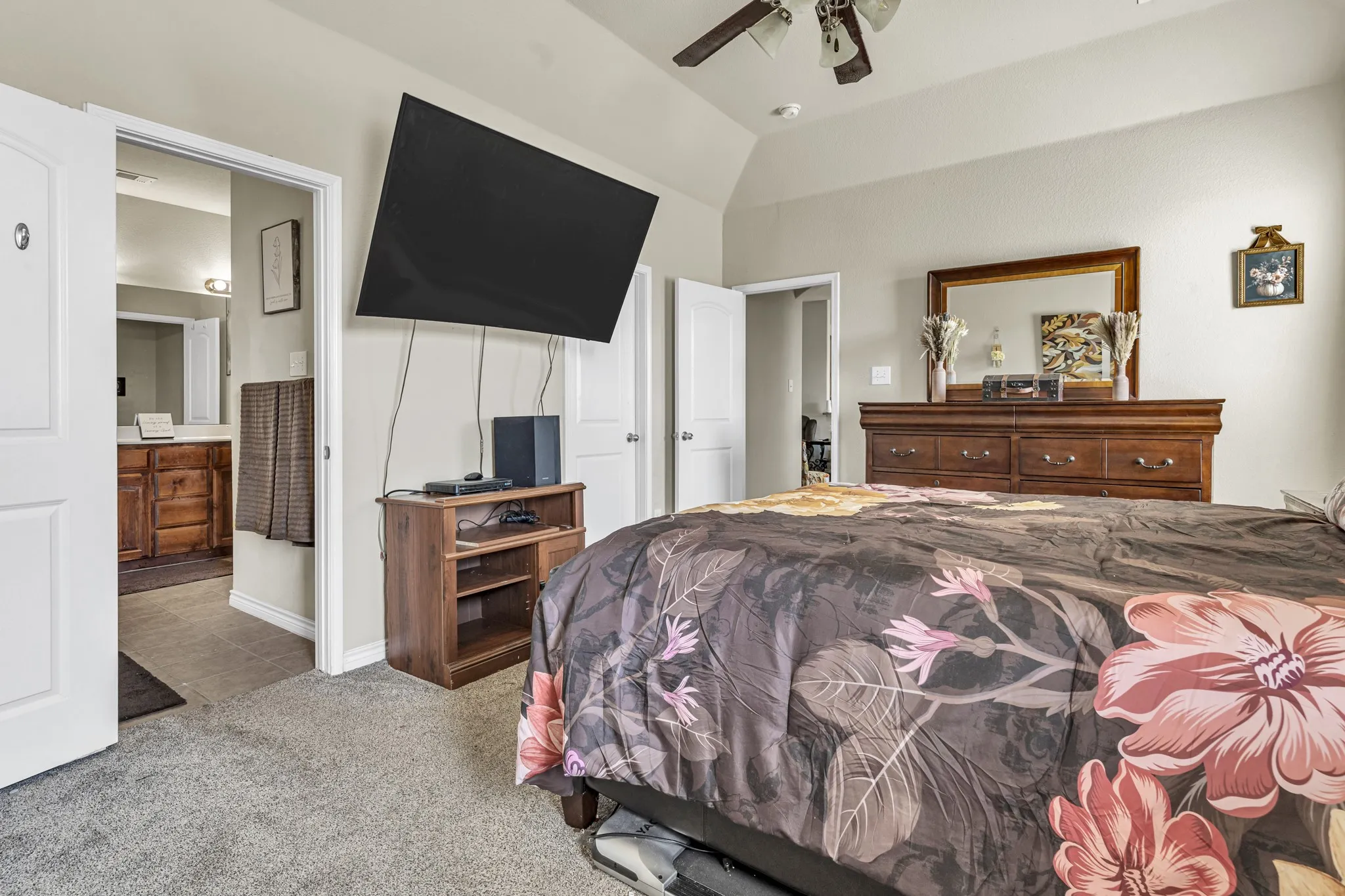 Vaulted ceiling, ceiling fan, carpet flooring, and an adjoining bathroom with a wood-finish vanity