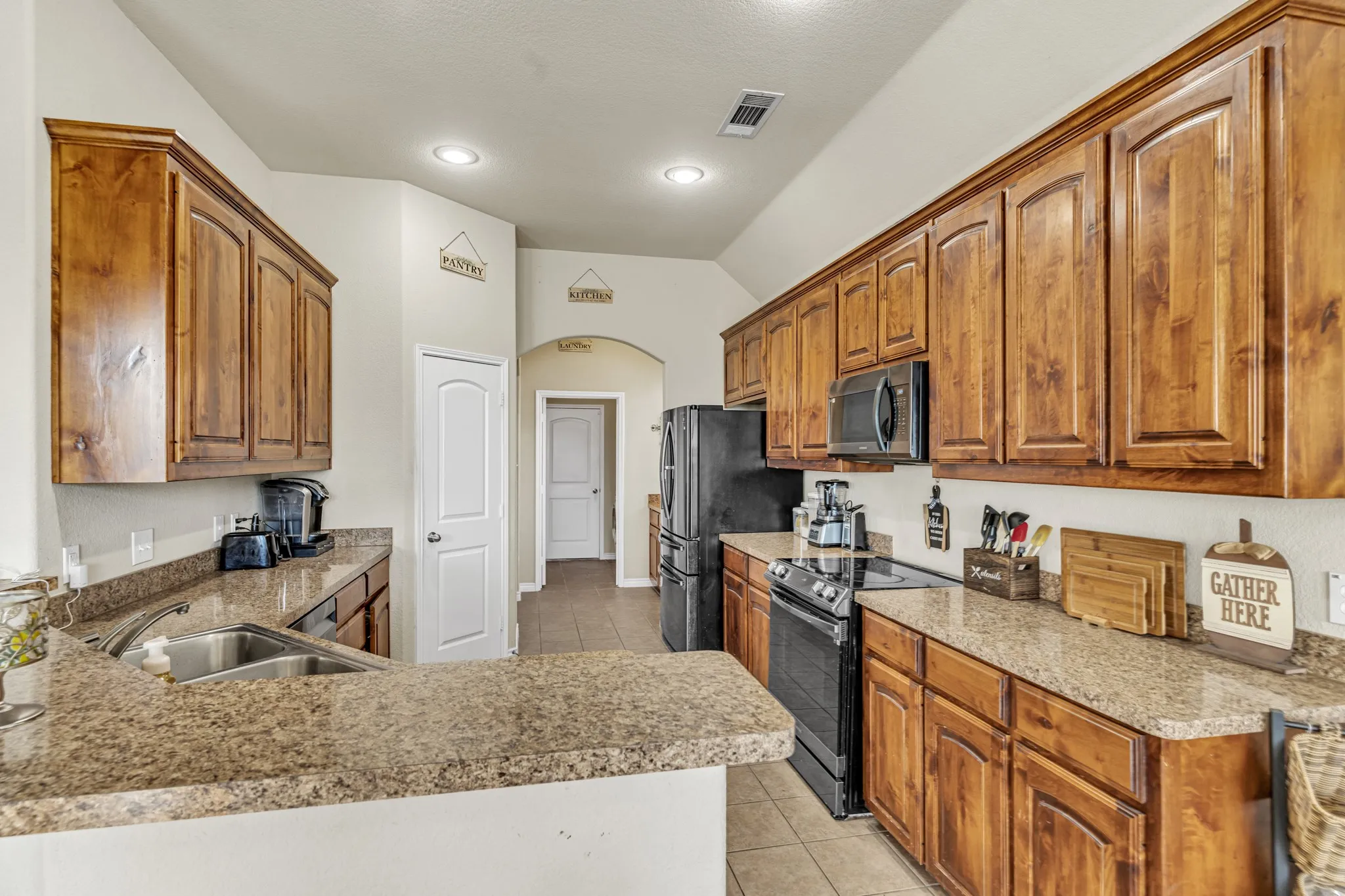 Kitchen featuring wood cabinetry, granite-style countertops, stainless steel sink, black appliances, and recessed lighting