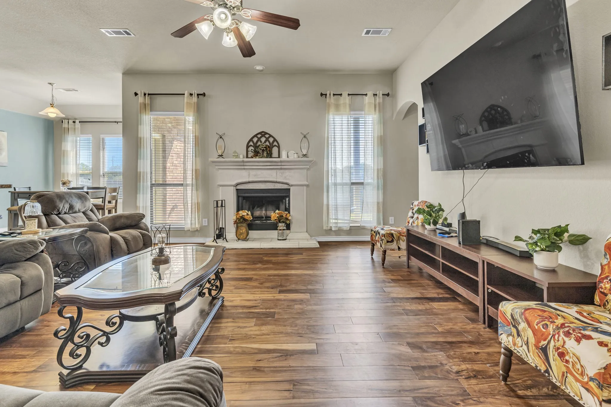 Living area featuring wood-finish flooring, a fireplace with a white mantel, and ceiling fan with integrated lighting