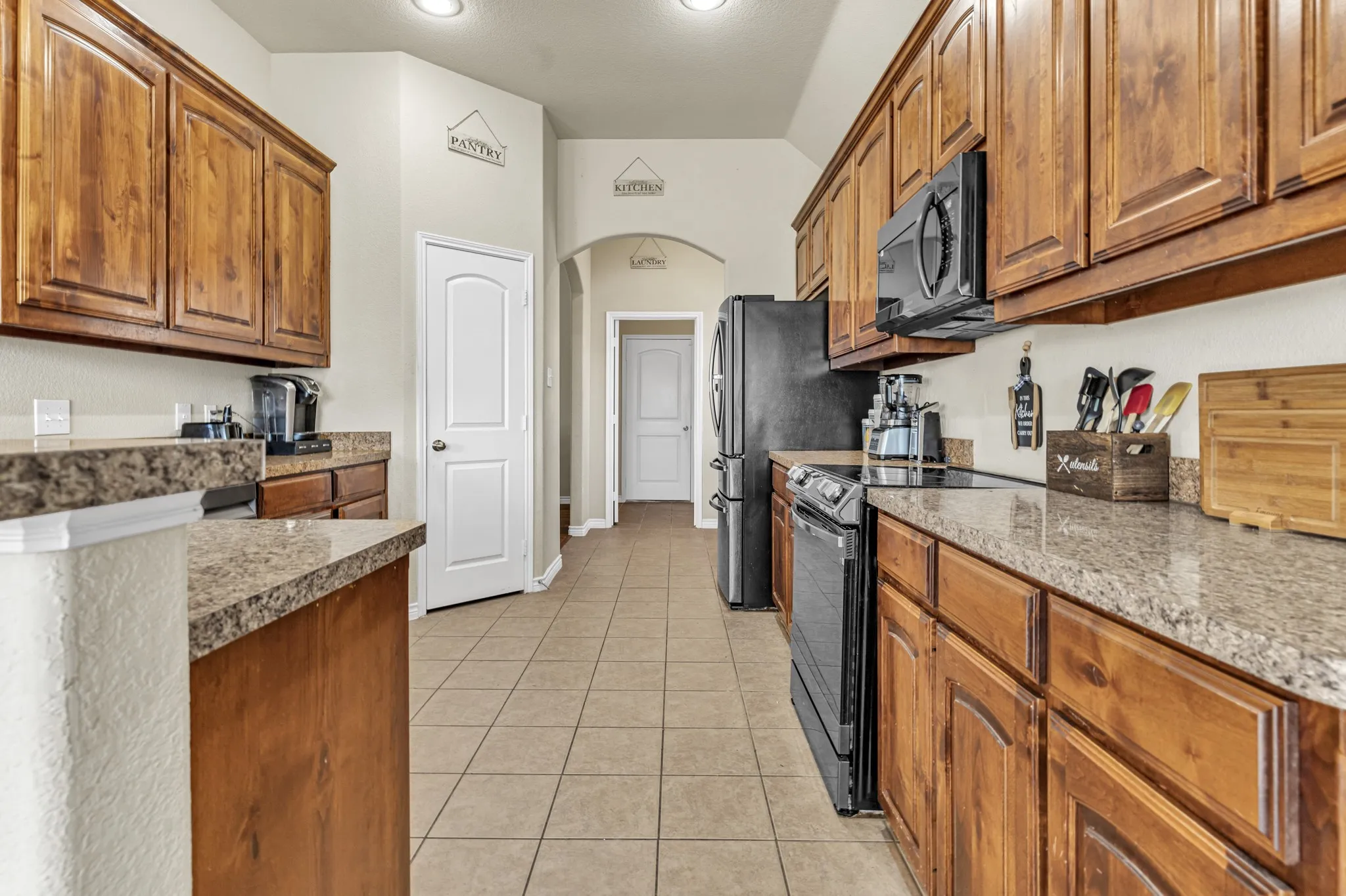 Warm wood cabinetry, granite-style countertops, tile flooring, and integrated black appliances