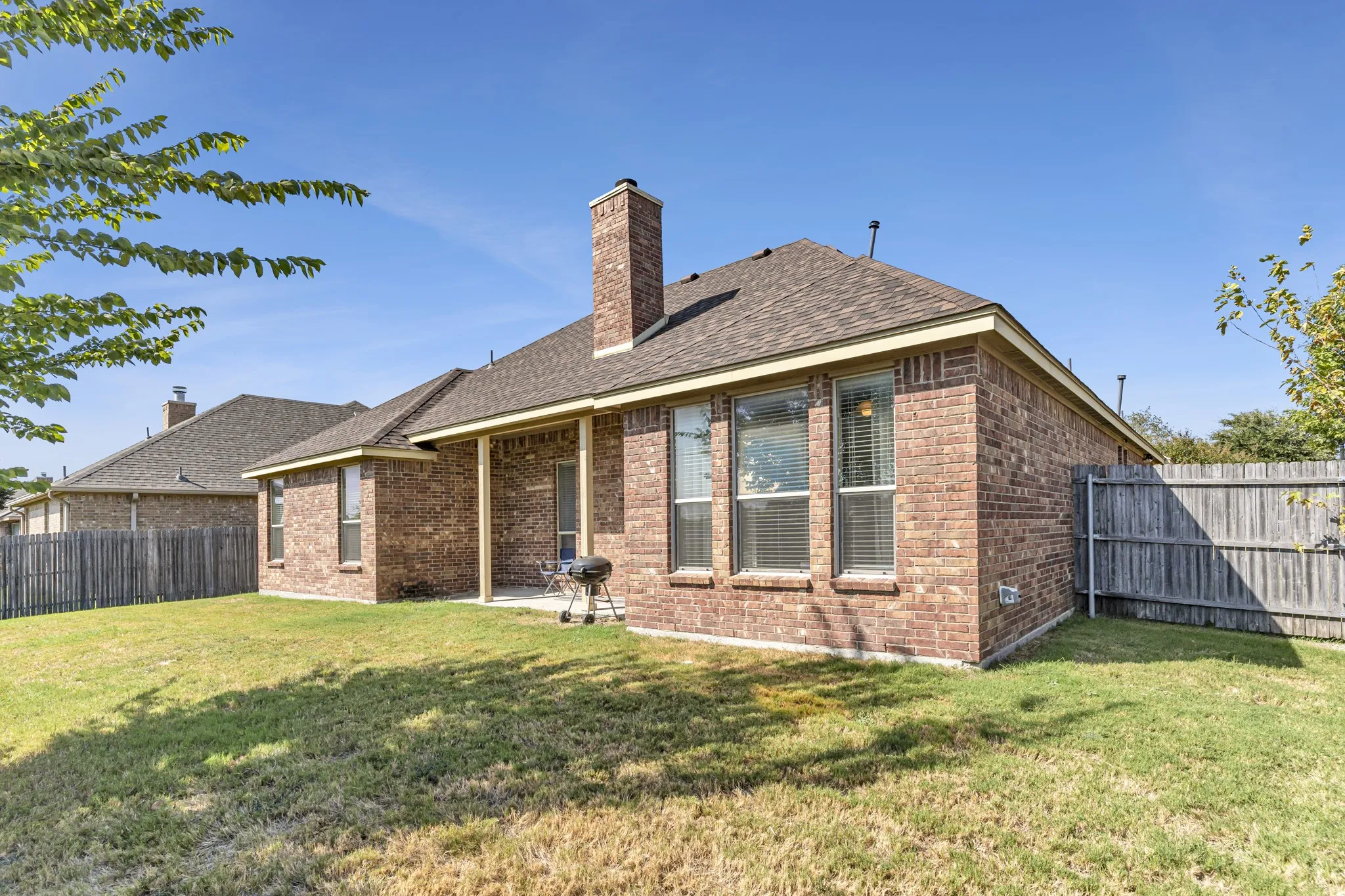 Brick exterior with a covered patio, fenced yard, and a shingled roof