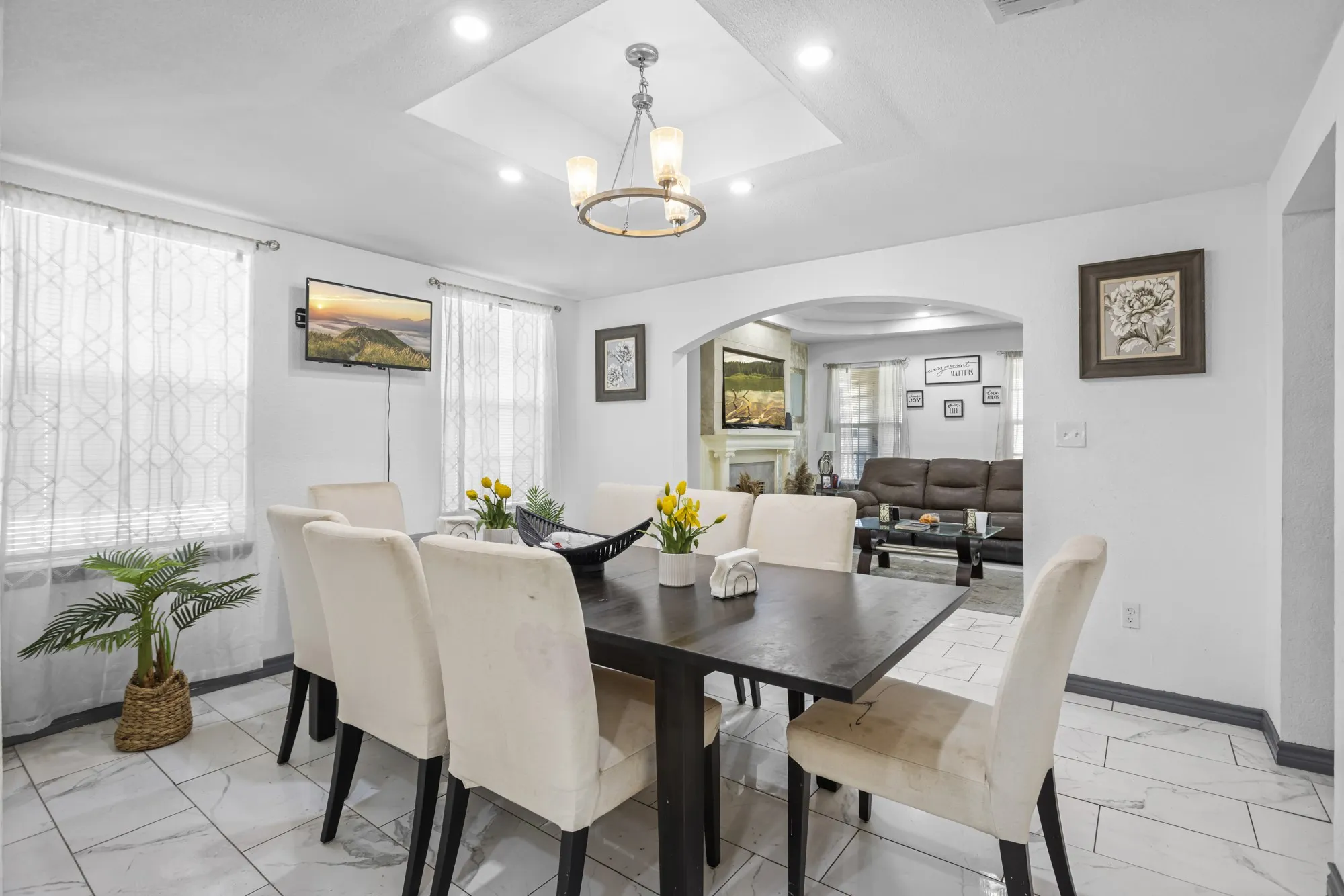 Dining room featuring arched walkways, light marble finish flooring, a chandelier, and a raised ceiling