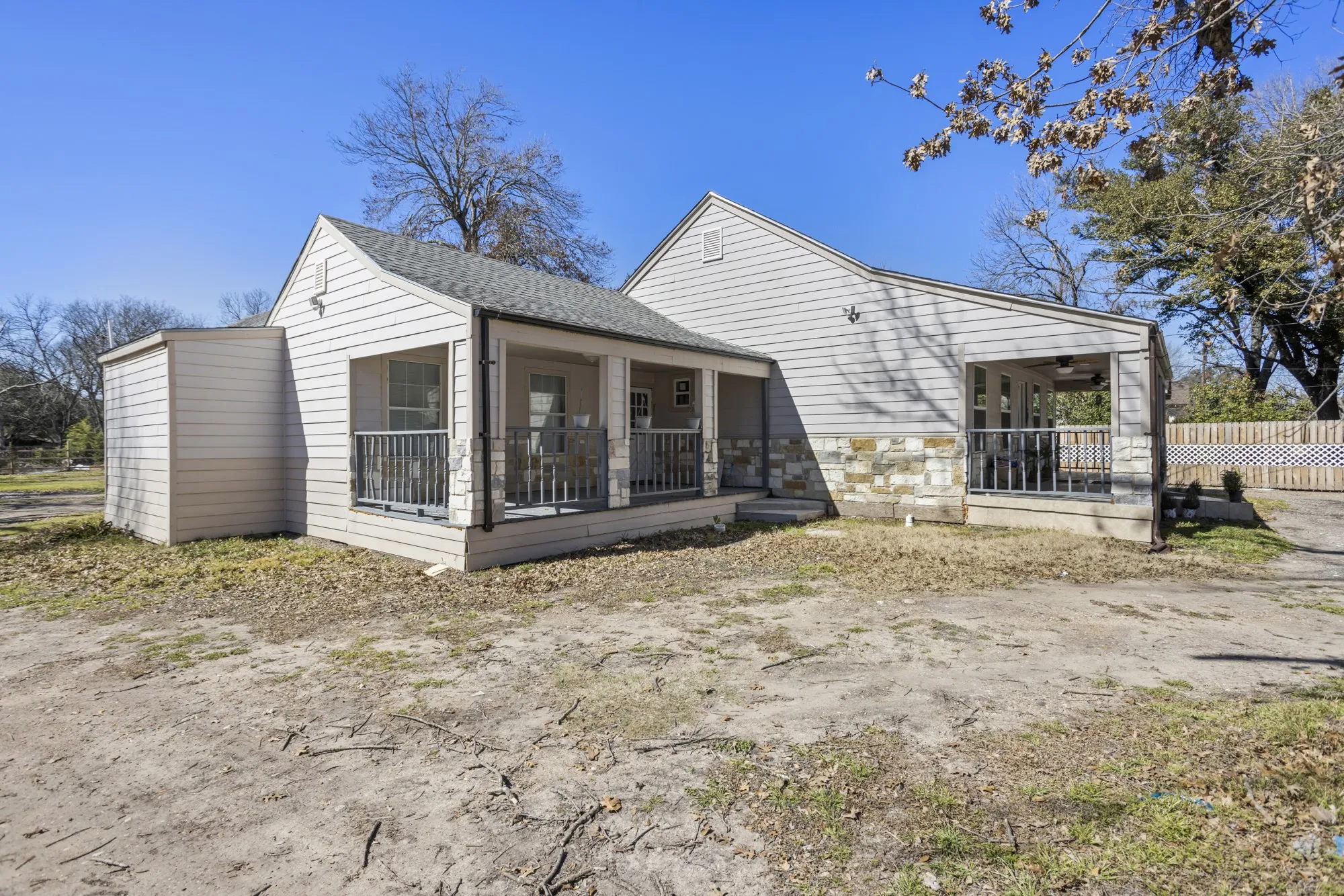 View of side of property featuring covered porch, stone siding, and a shingled roof
