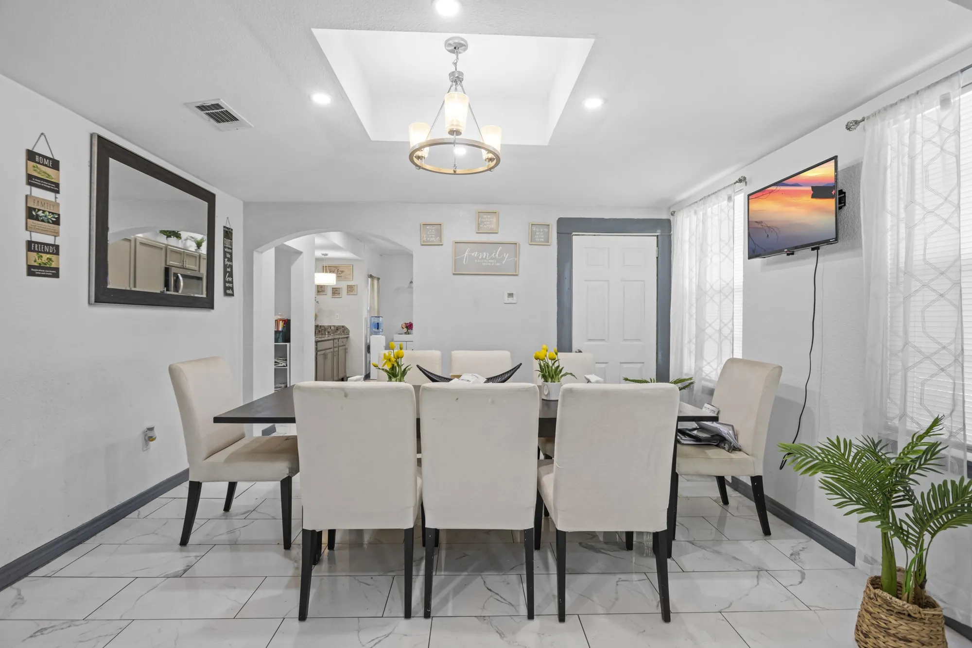 Dining room featuring arched walkways, a chandelier, a raised ceiling, recessed lighting, and light marble finish floors