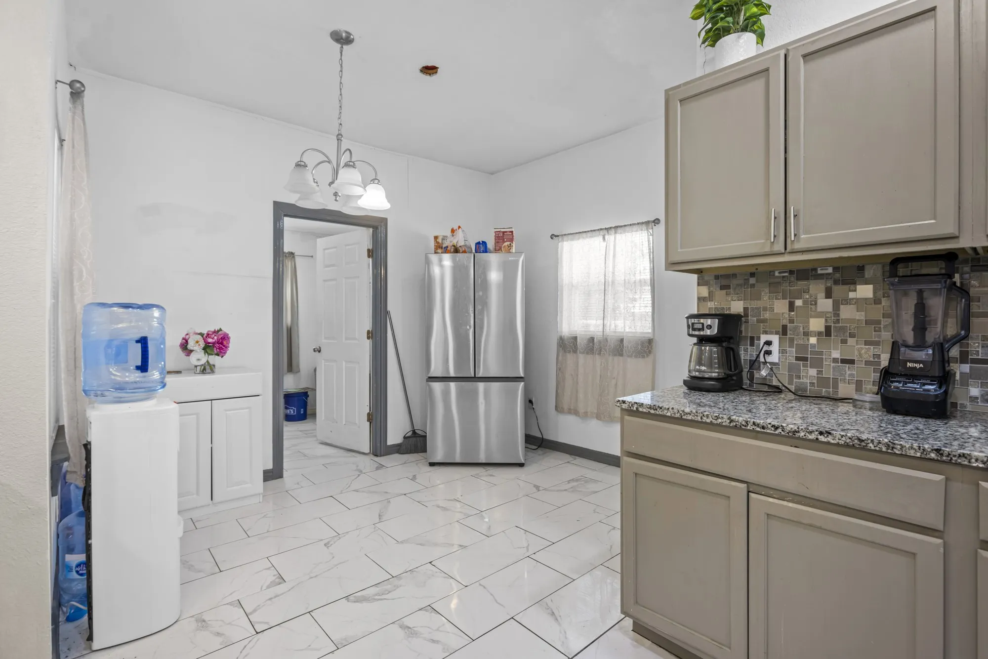 Kitchen featuring freestanding refrigerator, gray cabinetry, a chandelier, light marble finish flooring, and decorative backsplash