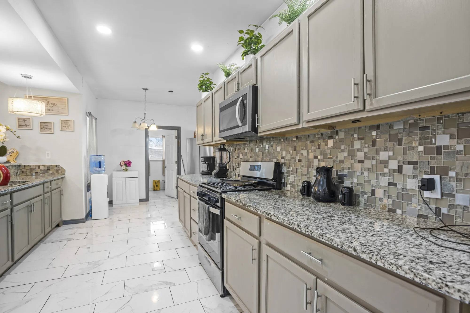 Kitchen with appliances with stainless steel finishes, decorative backsplash, light marble finish floors, hanging light fixtures, and recessed lighting