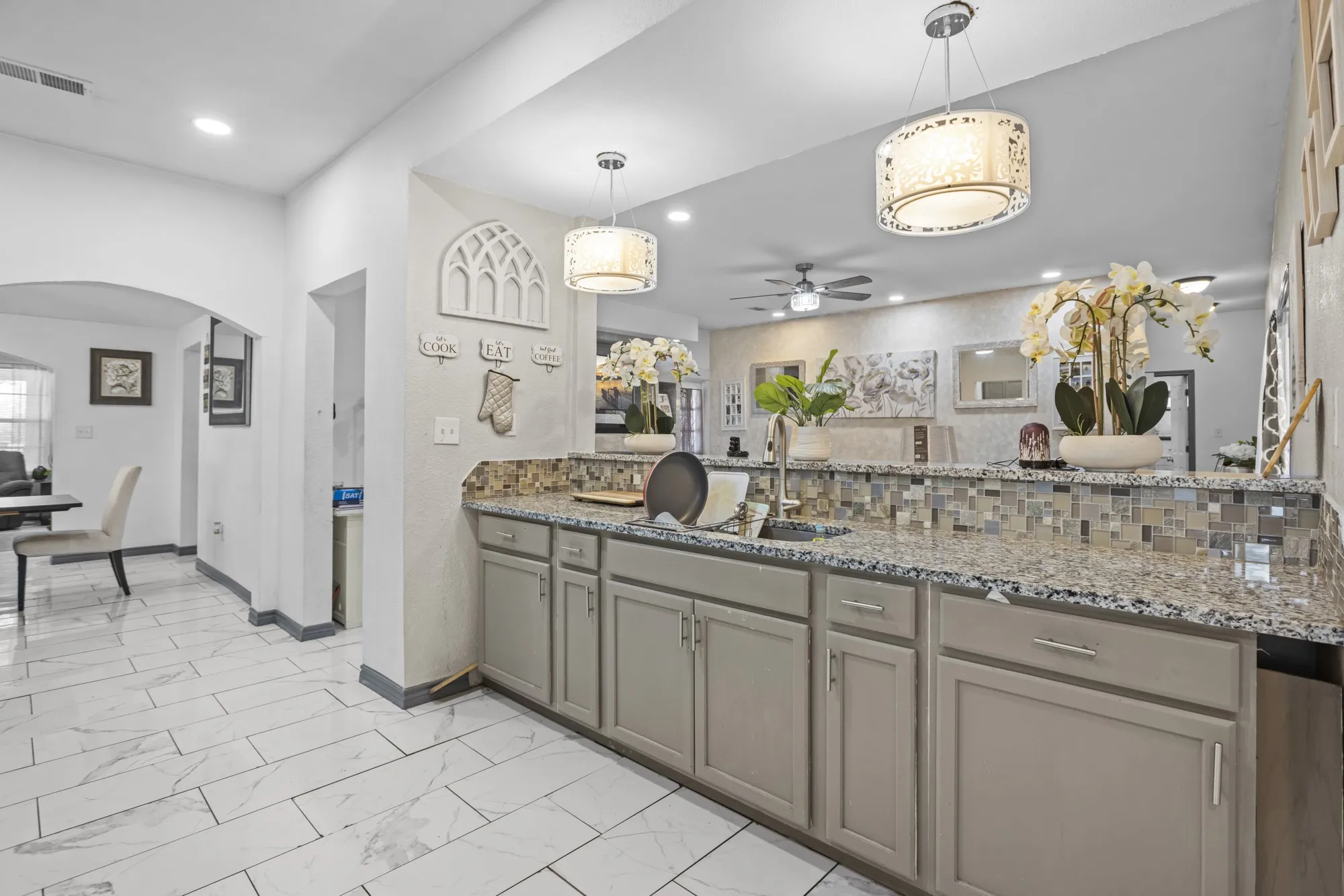 Kitchen featuring arched walkways, gray cabinetry, ceiling fan, light marble finish floors, and light stone countertops