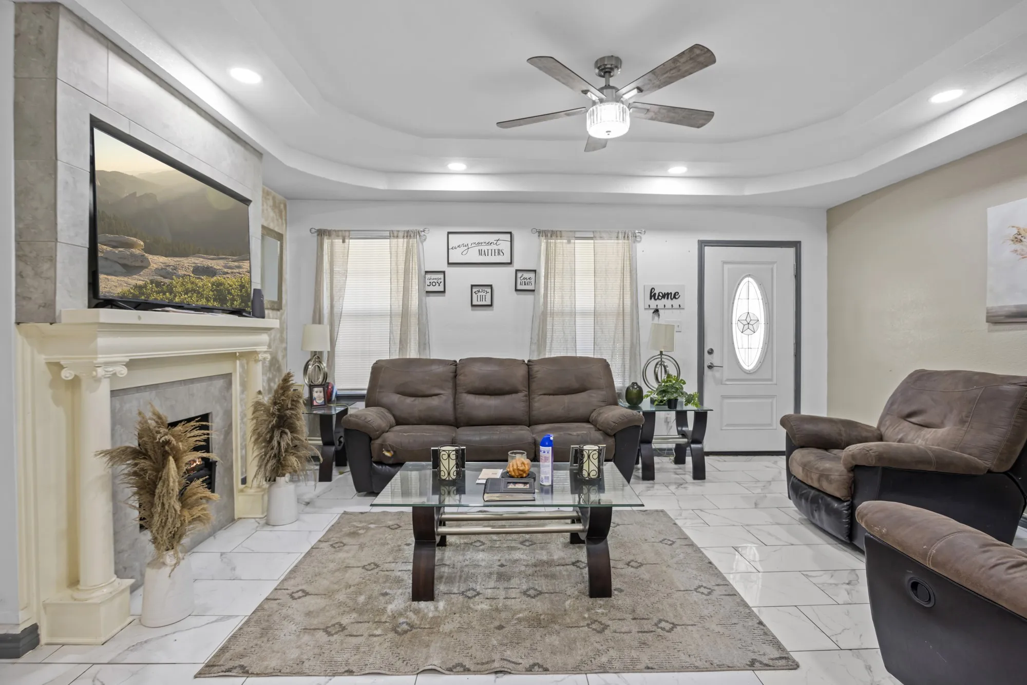 Living area with recessed lighting, a raised ceiling, ceiling fan, light marble finish flooring, and a fireplace