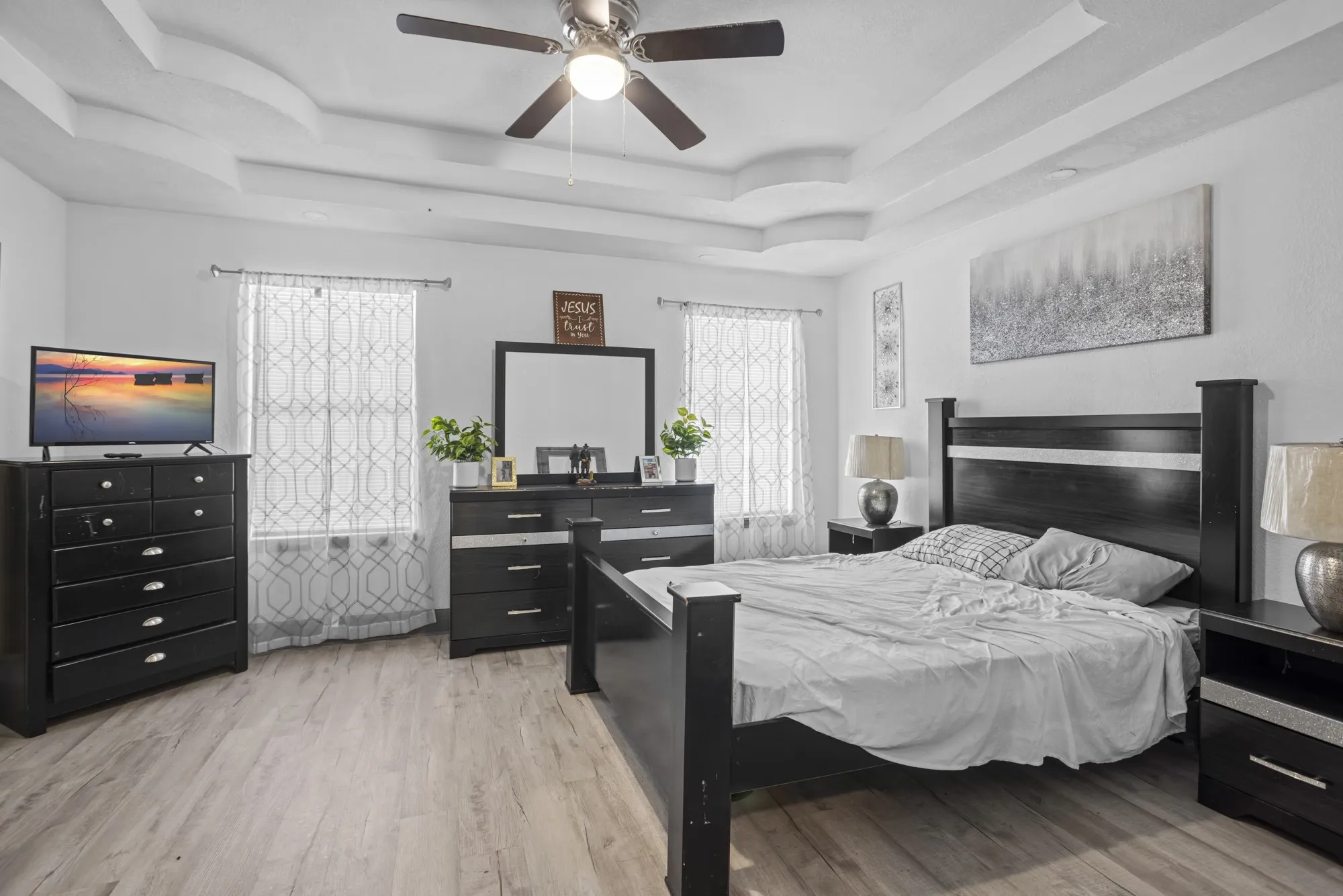 Bedroom featuring a raised ceiling, light wood-style floors, and ceiling fan