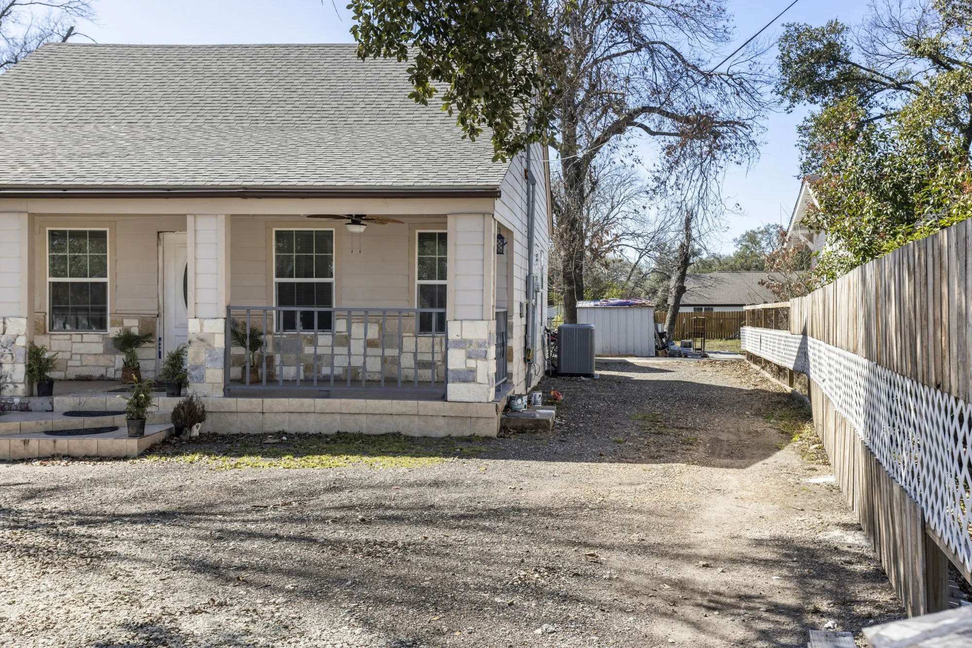 View of front of property with a shingled roof, covered porch, ceiling fan, gravel driveway, and stone siding