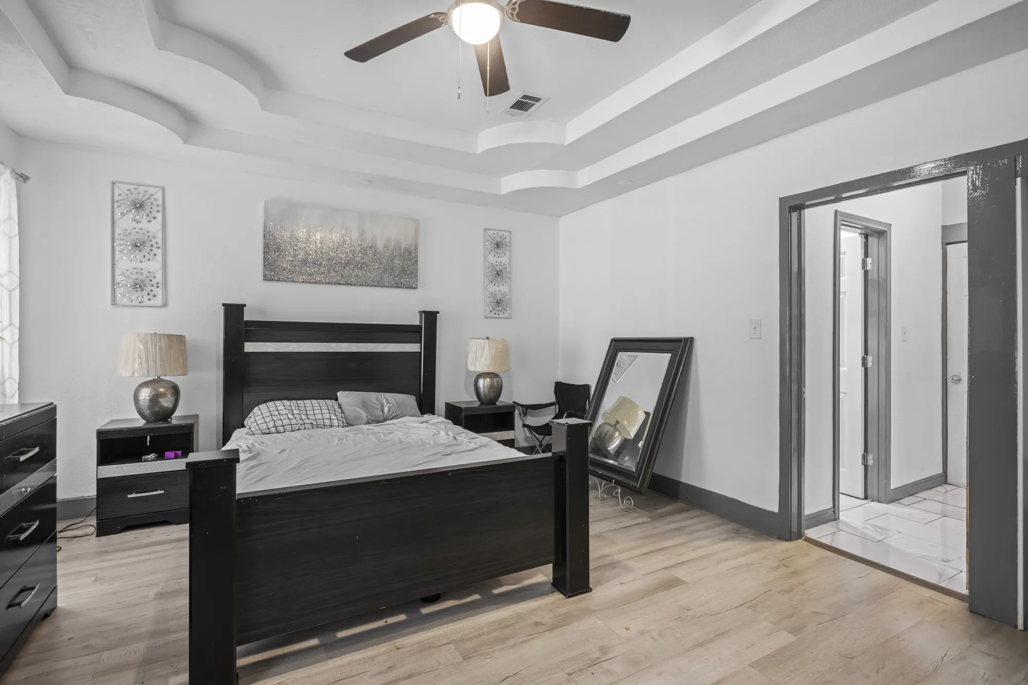 Bedroom featuring a raised ceiling, light wood finished floors, and a ceiling fan