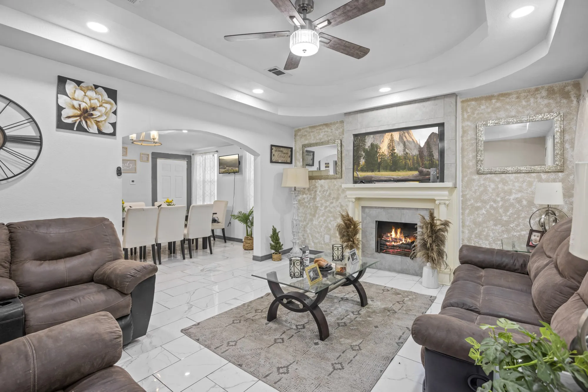 Living room featuring a raised ceiling, recessed lighting, arched walkways, ceiling fan, and a large fireplace