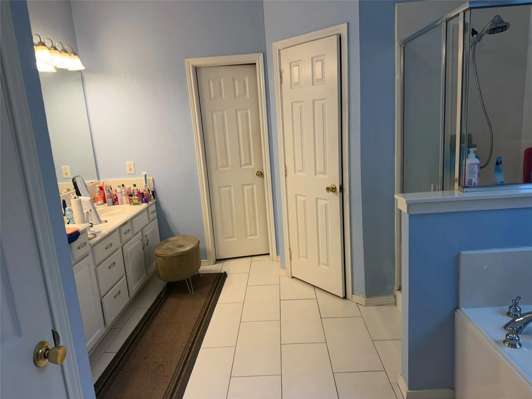 White tile flooring, a built-in double vanity with ample storage, a glass-enclosed shower, and a built-in tub