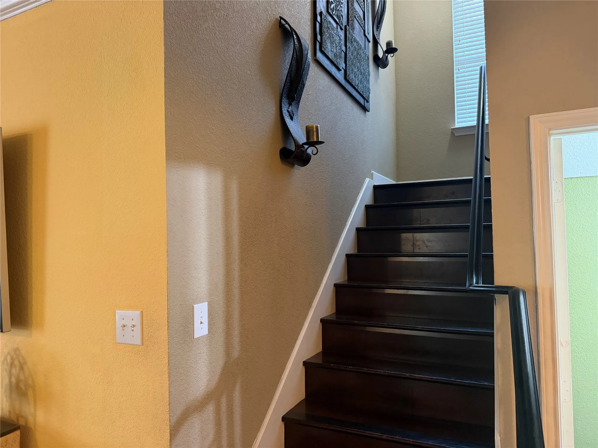 Staircase featuring dark wood-finish treads and risers, a black handrail, and a window with blinds