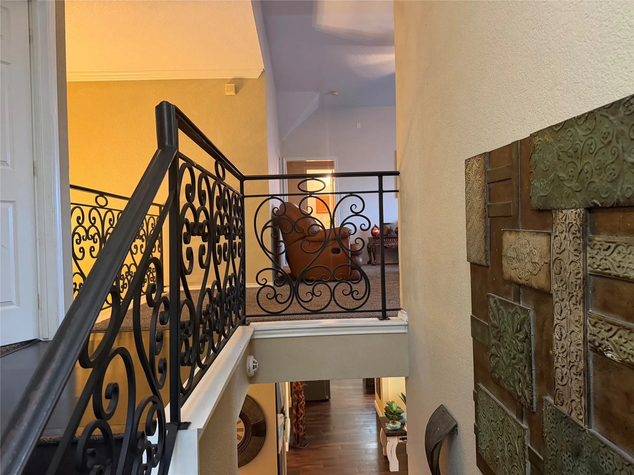 Decorative wrought iron stair railing, upper-level landing, textured wall paneling, crown molding