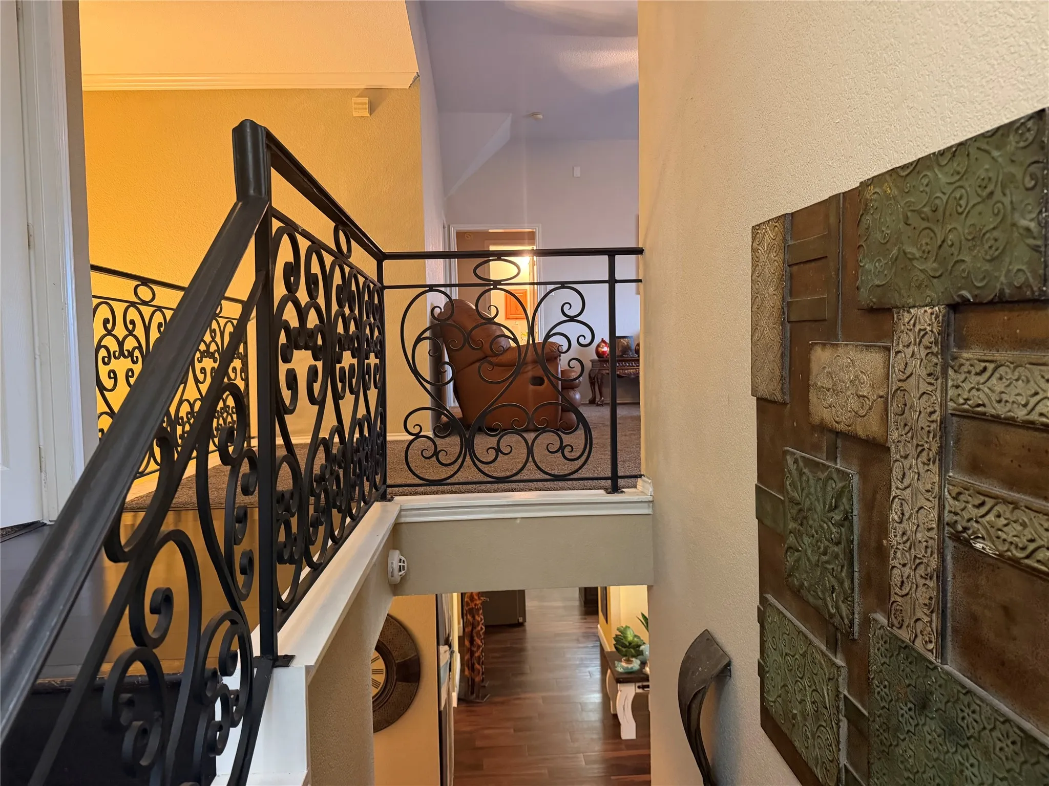 Wrought iron balustrade with intricate scrollwork, carpeted stair treads, and wood-finish flooring visible below