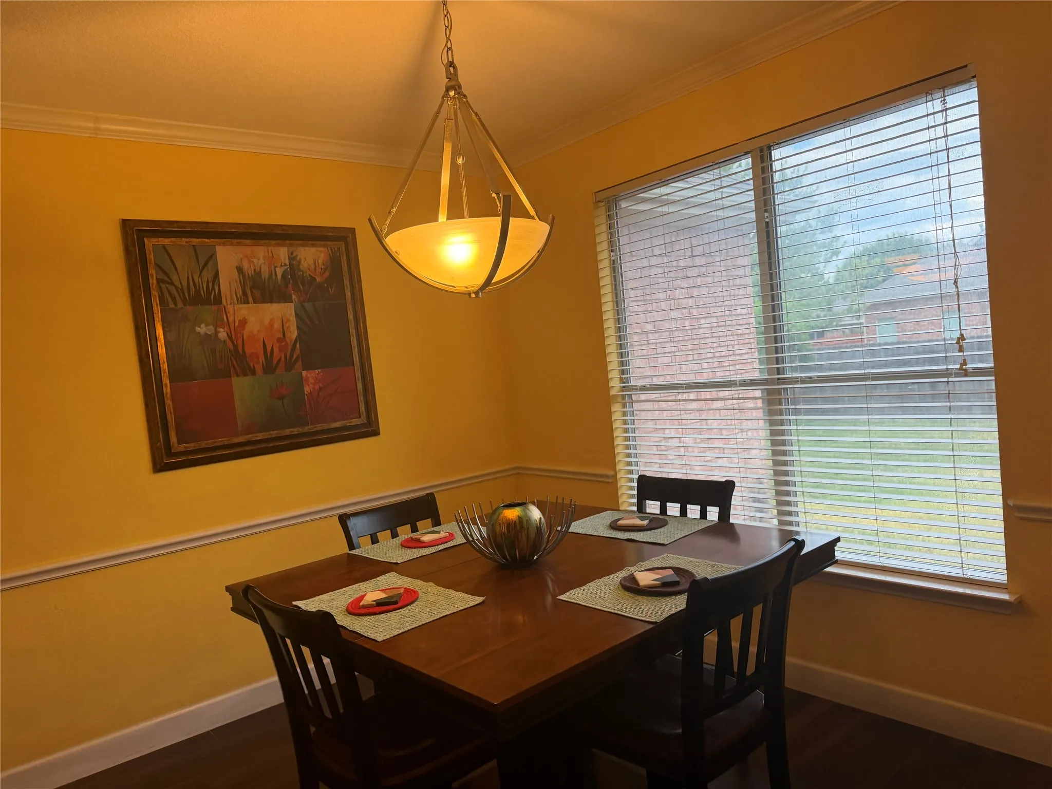 Crown molding, chair rail molding, large window, pendant light fixture, dark wood-finish flooring