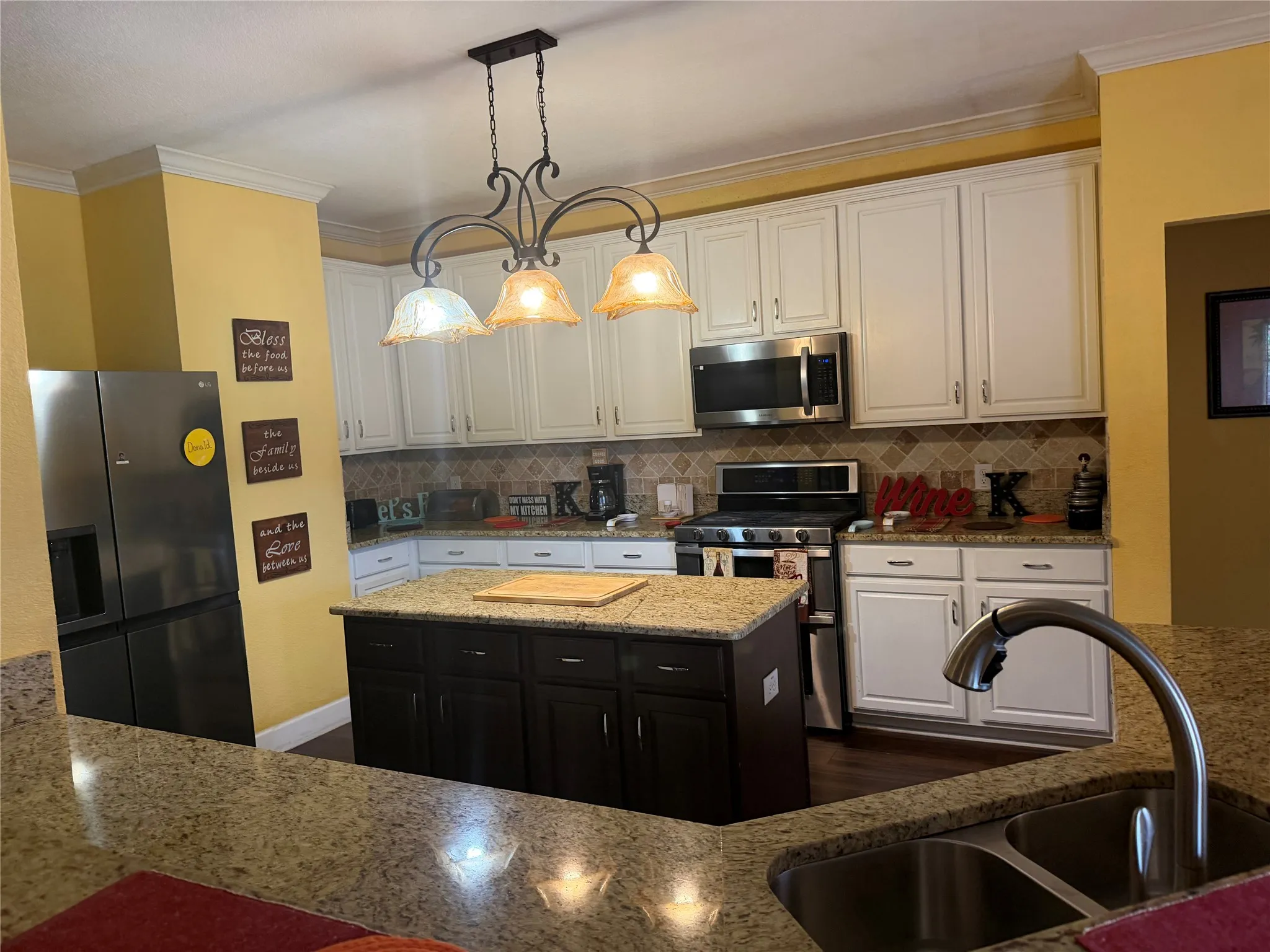 Kitchen featuring white cabinetry, a central island with dark wood-finish cabinetry, stainless steel appliances, and multi-toned backsplash