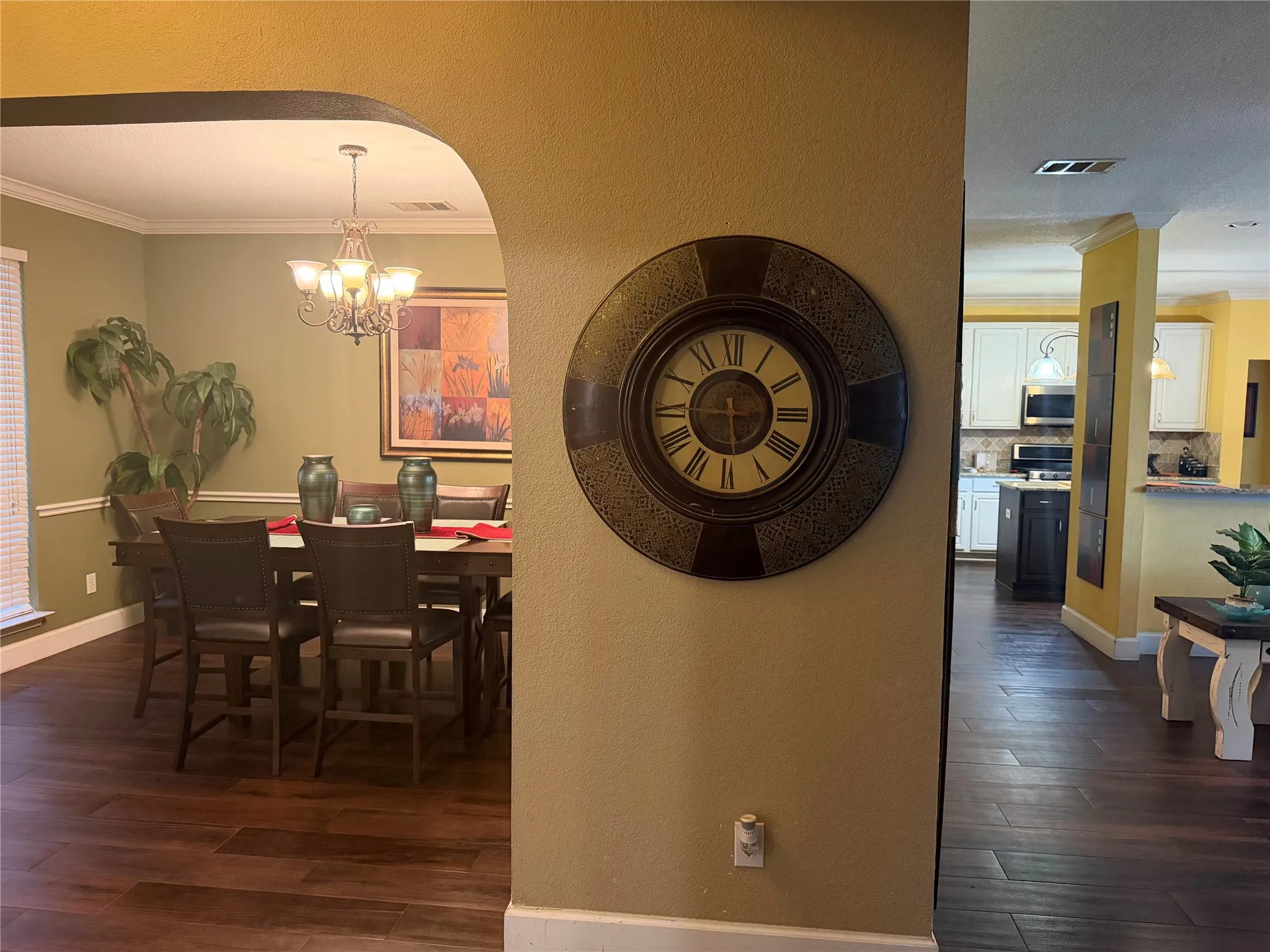 Wood-finish flooring throughout, arched entryway, crown molding, and a chandelier lighting fixture