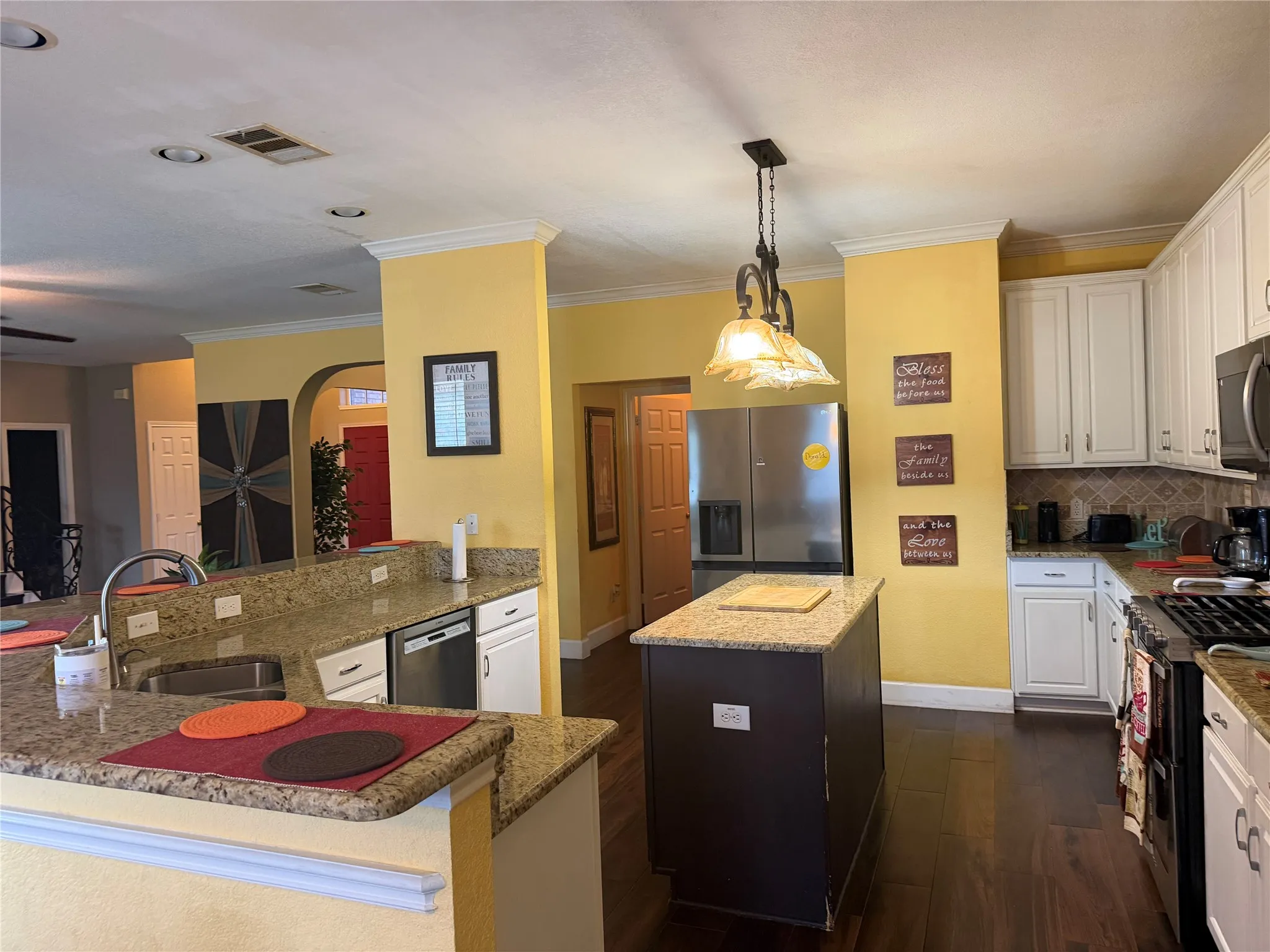 Kitchen featuring wood-finish flooring, granite countertops, white cabinetry, a central island, and stainless steel appliances