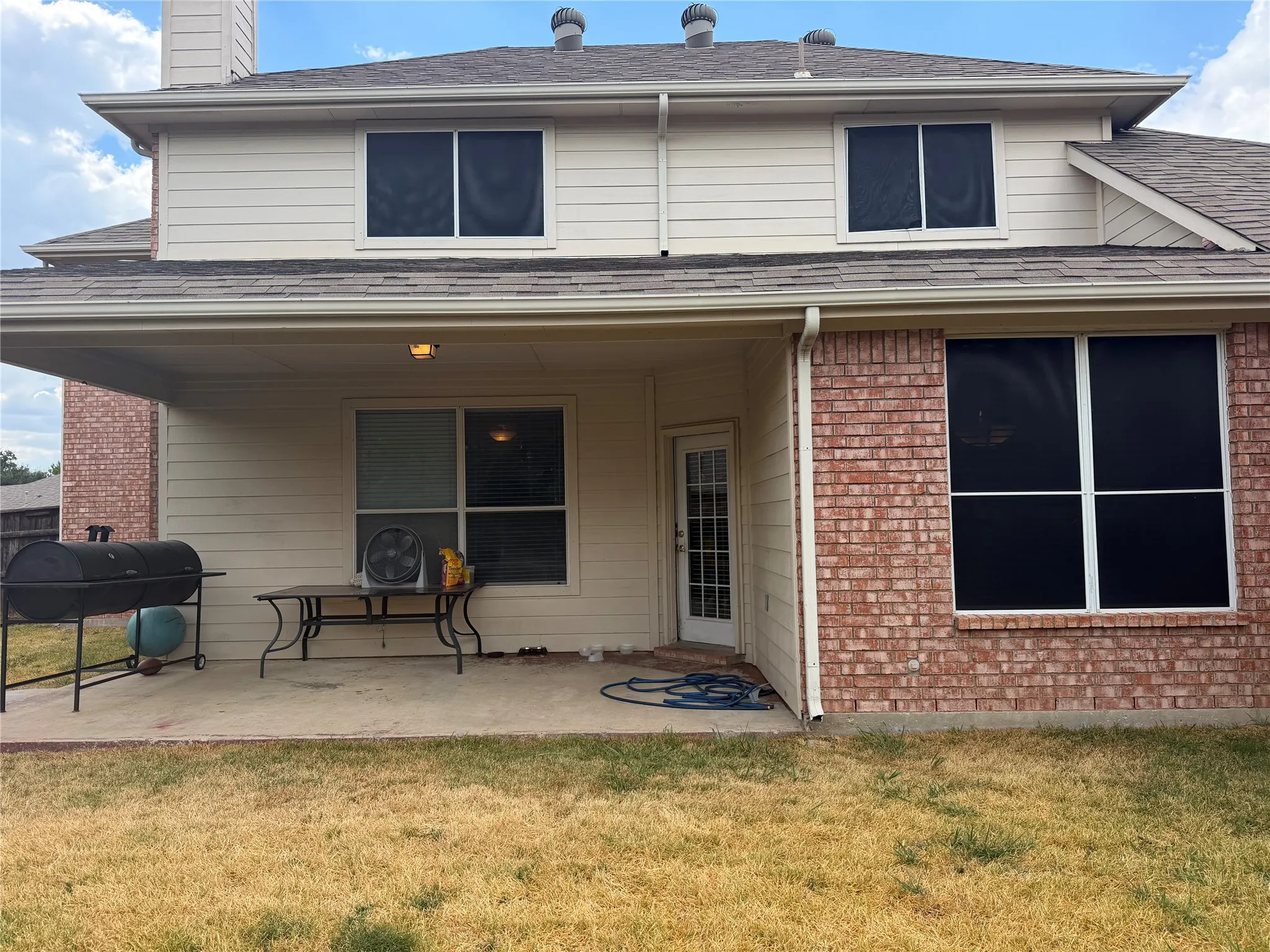 Rear exterior featuring a covered patio, brick and siding facade, and multiple windows