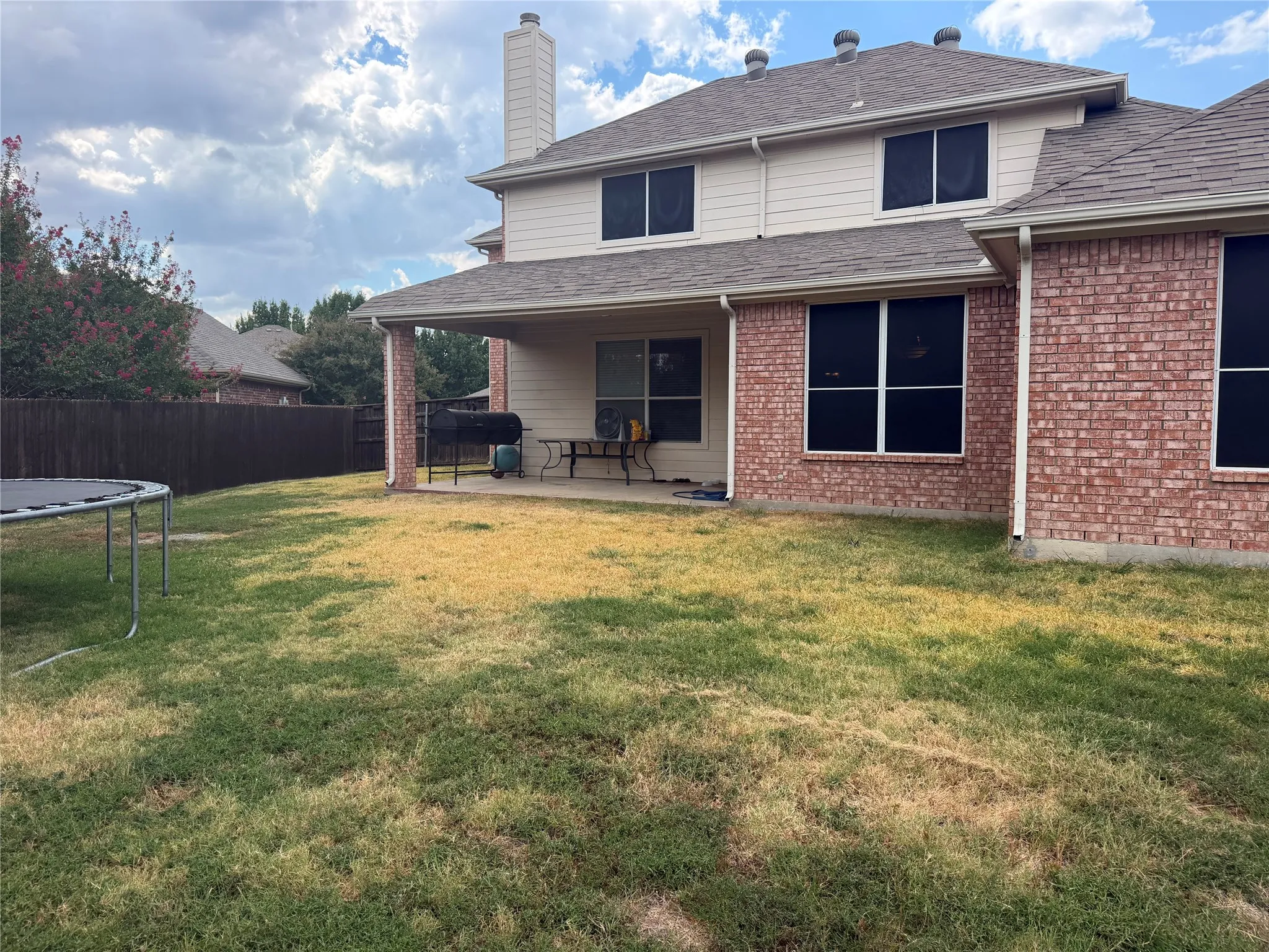 Expansive backyard featuring a covered patio with brick columns, a privacy fence, and a two-story exterior with brick and siding finishes