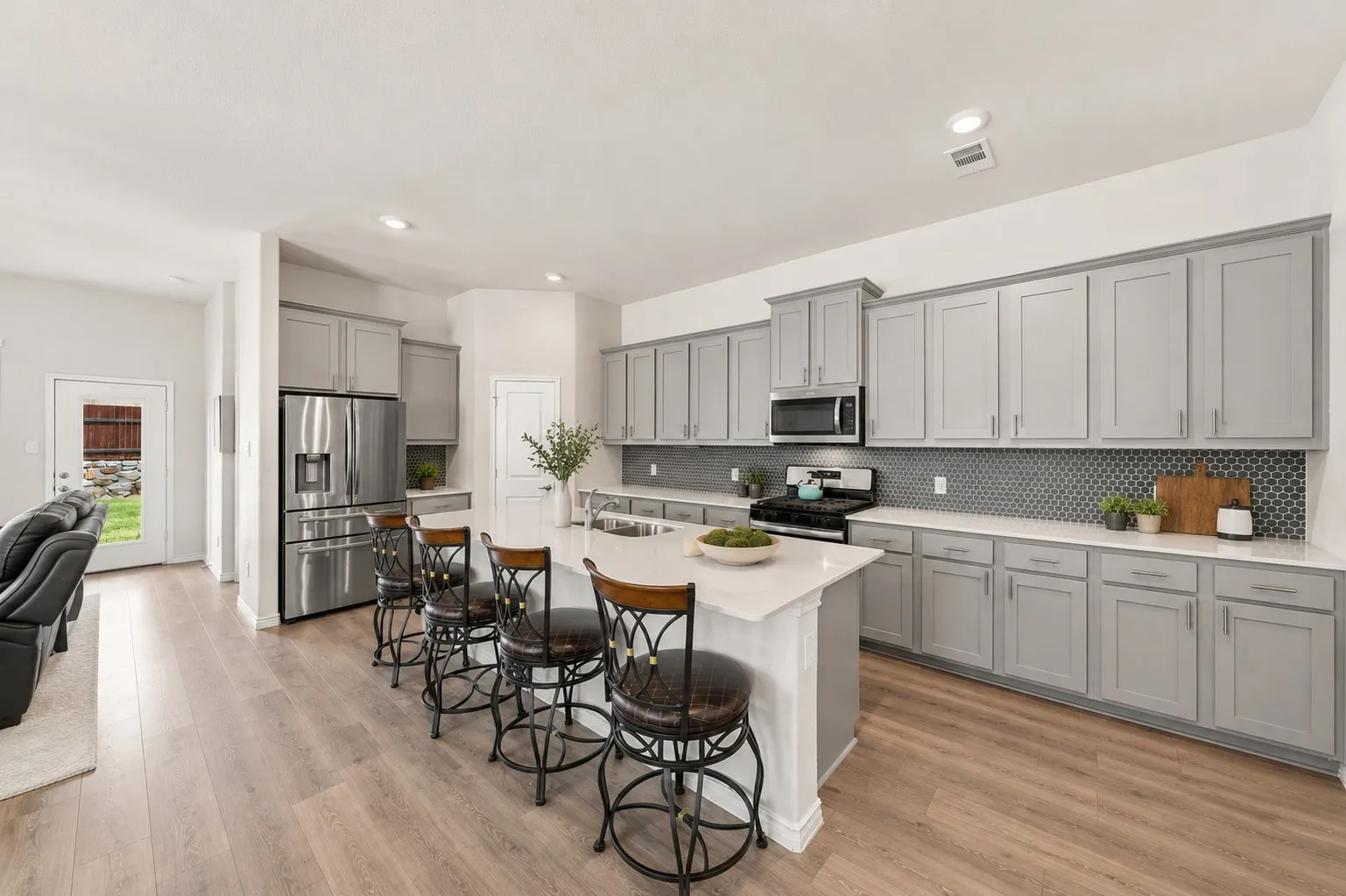 Spacious kitchen featuring an expansive island, light grey cabinetry, white countertops, stainless steel appliances, and wood-finish flooring