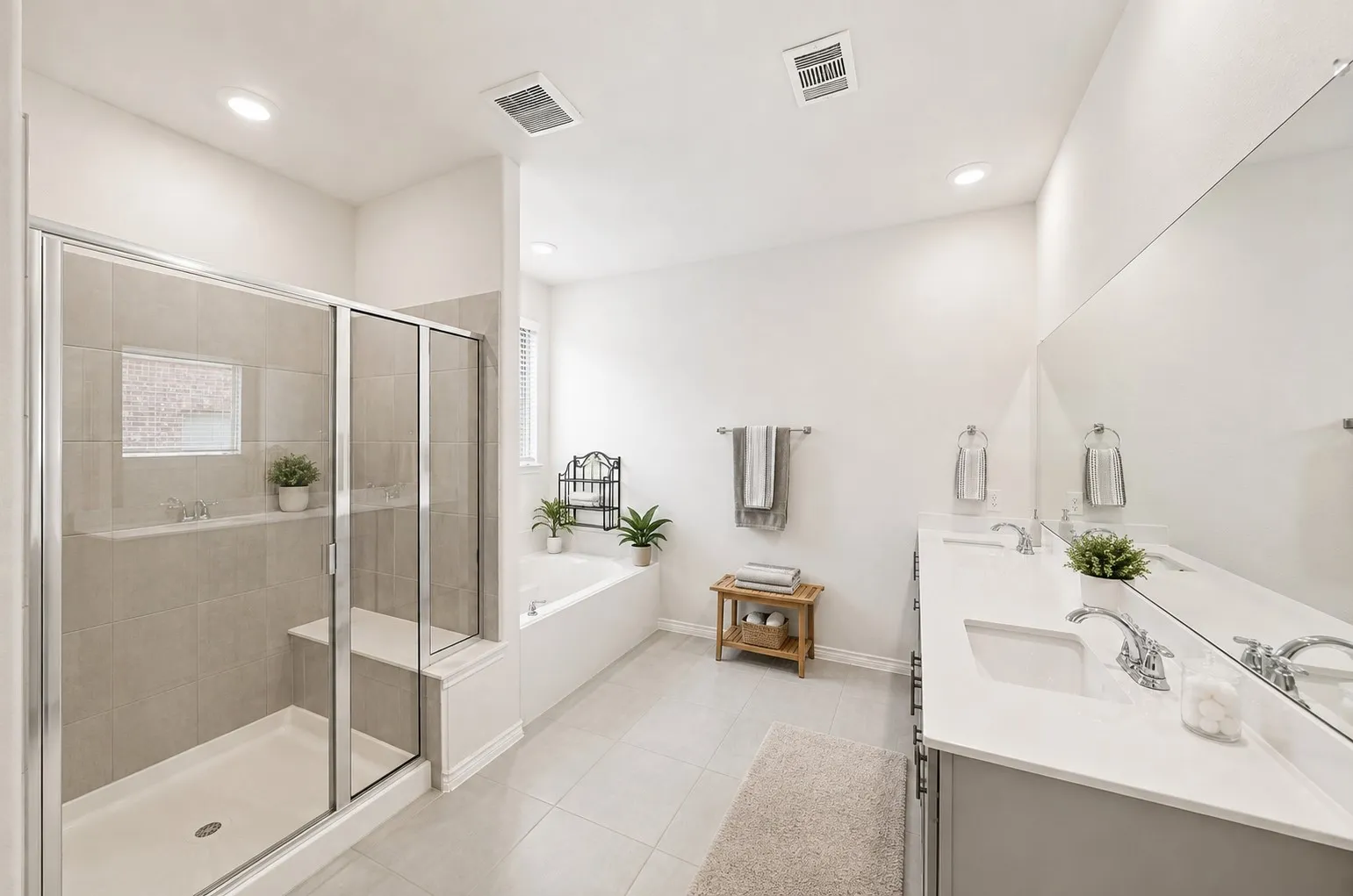 Dual vanity with undermount sinks and chrome fixtures, large frameless mirror, separate shower with clear glass enclosure, built-in shower bench, and a spacious soaking tub