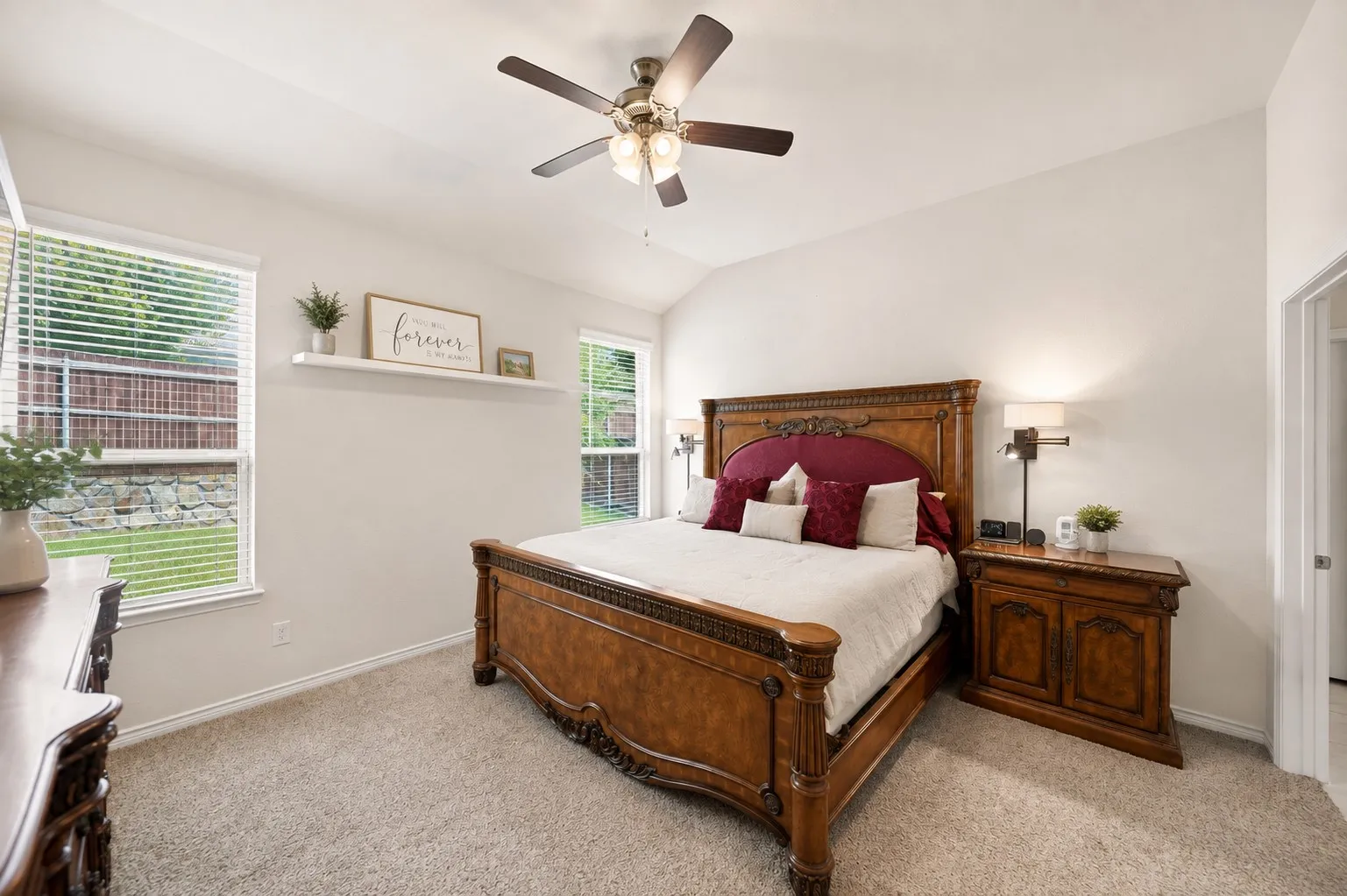 Vaulted ceiling, two windows, ceiling fan, neutral carpet flooring, and a floating wall shelf