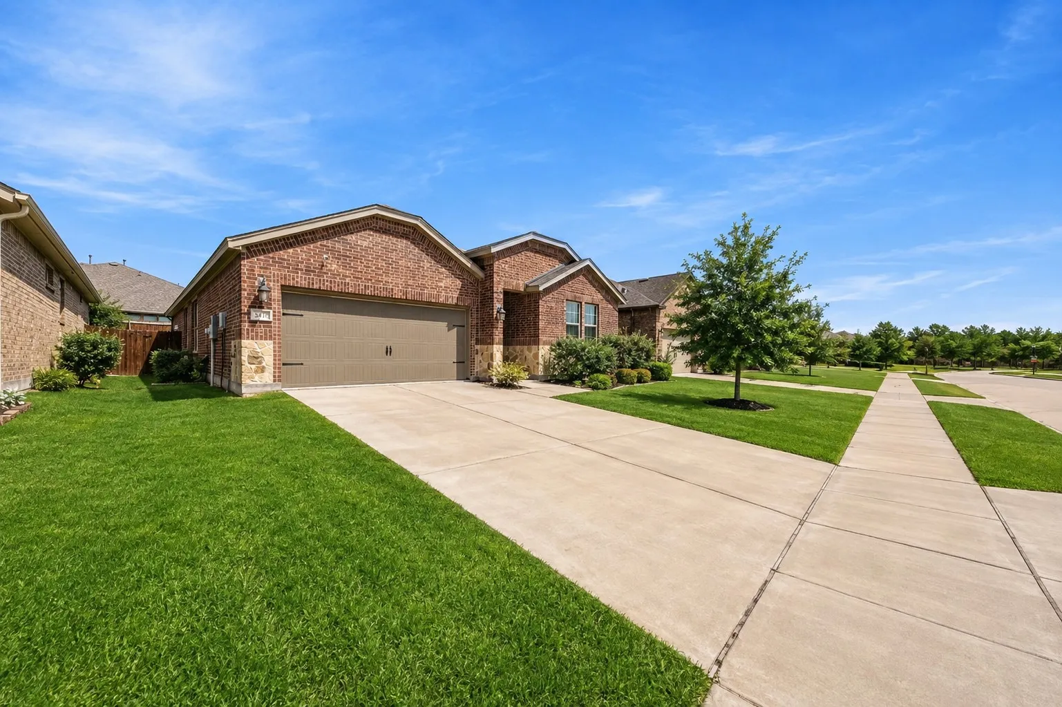 Brick exterior with stone accents, attached garage with a double door, concrete driveway, and a front lawn with foundational landscaping