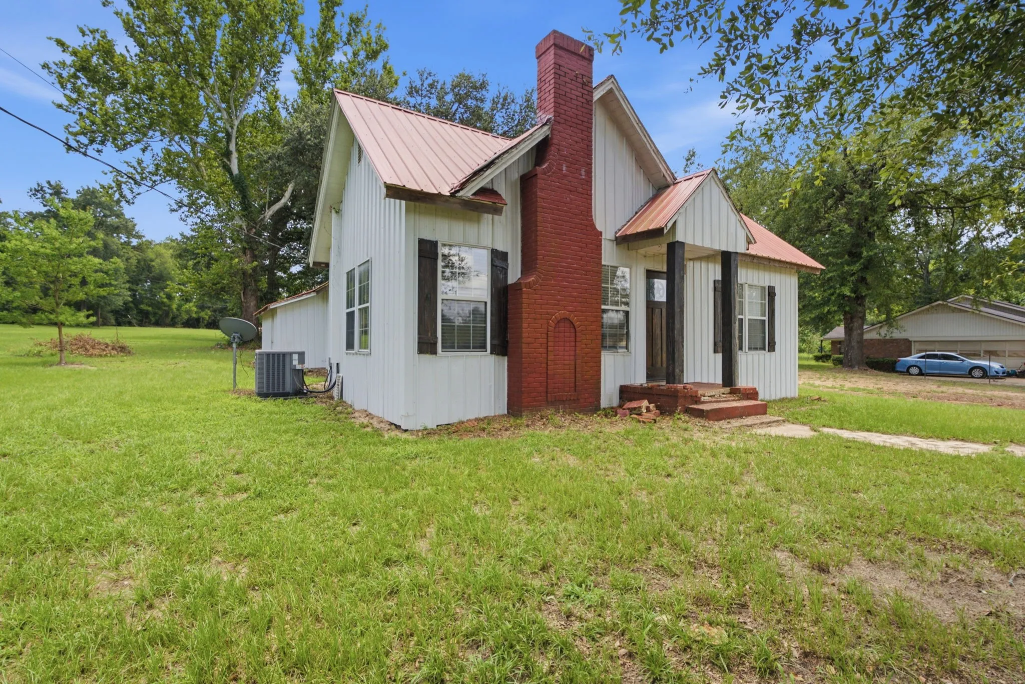 White vertical siding exterior with a red metal roof, a prominent brick chimney, and a covered entry