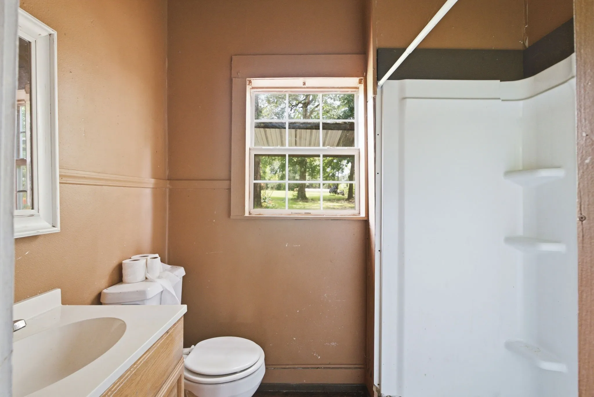 Bathroom featuring a vanity with an integrated sink, a toilet, a window with exterior views, and a white shower stall with built-in shelving