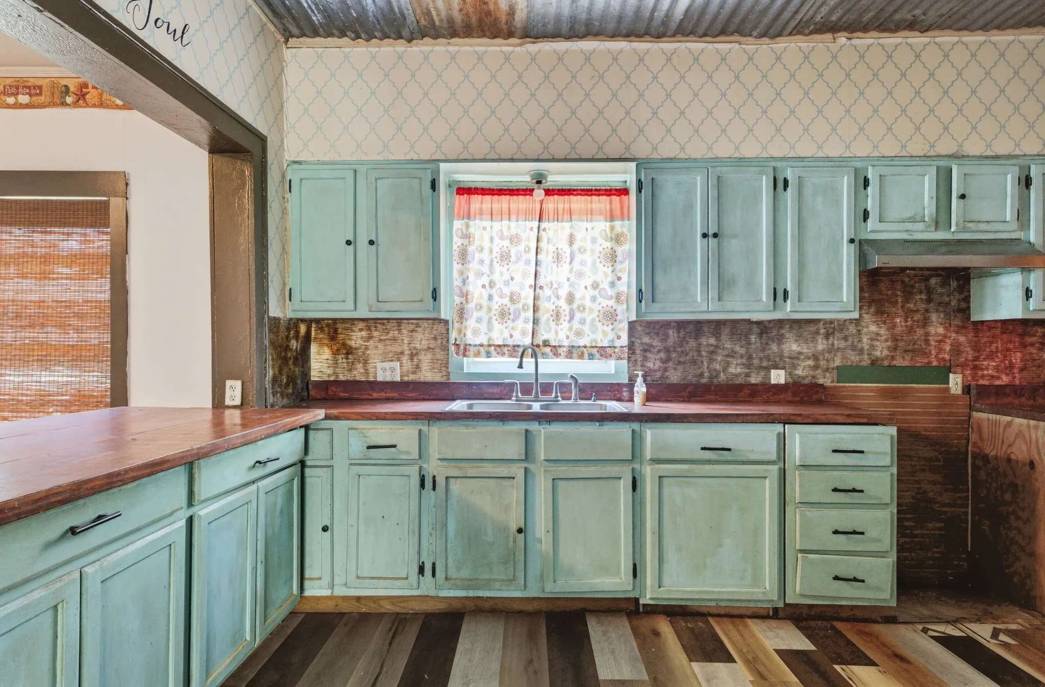 Kitchen featuring distressed blue cabinetry, wood-finish countertops, stainless steel sink, a corrugated metal ceiling, and patterned wallpaper