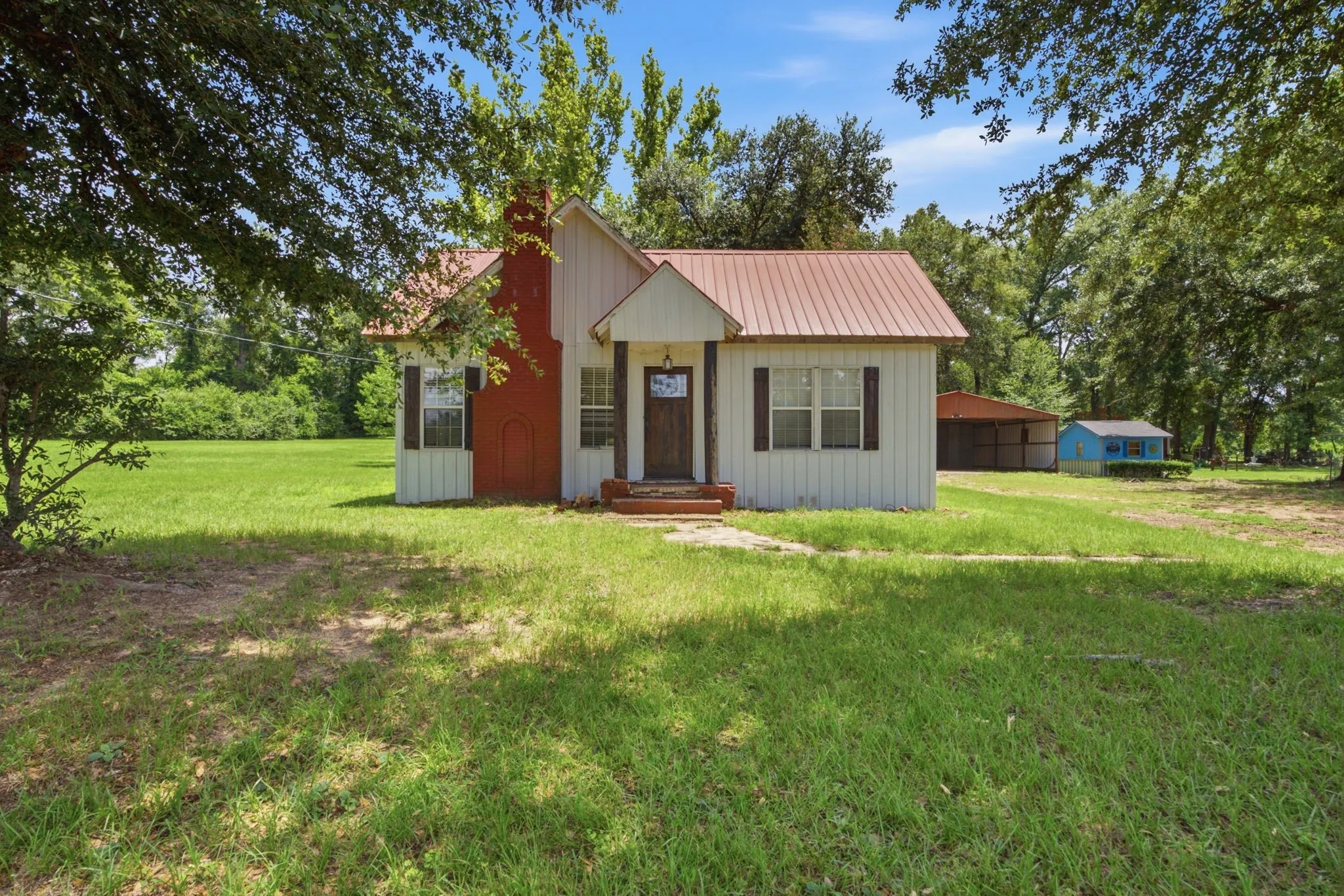 White siding exterior with a red metal roof and red brick chimney
