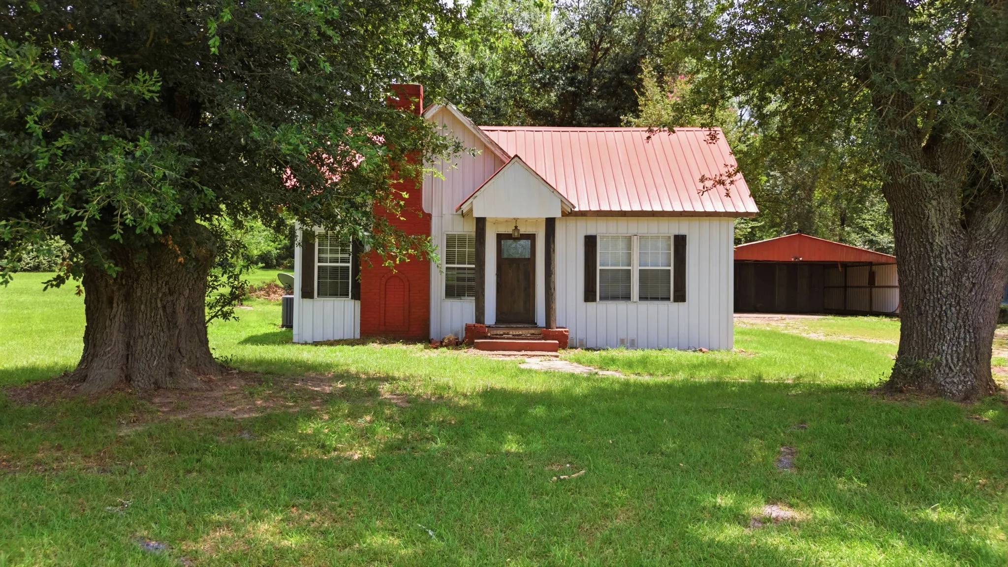 White siding exterior with a red metal roof, chimney, and dark wood shutters