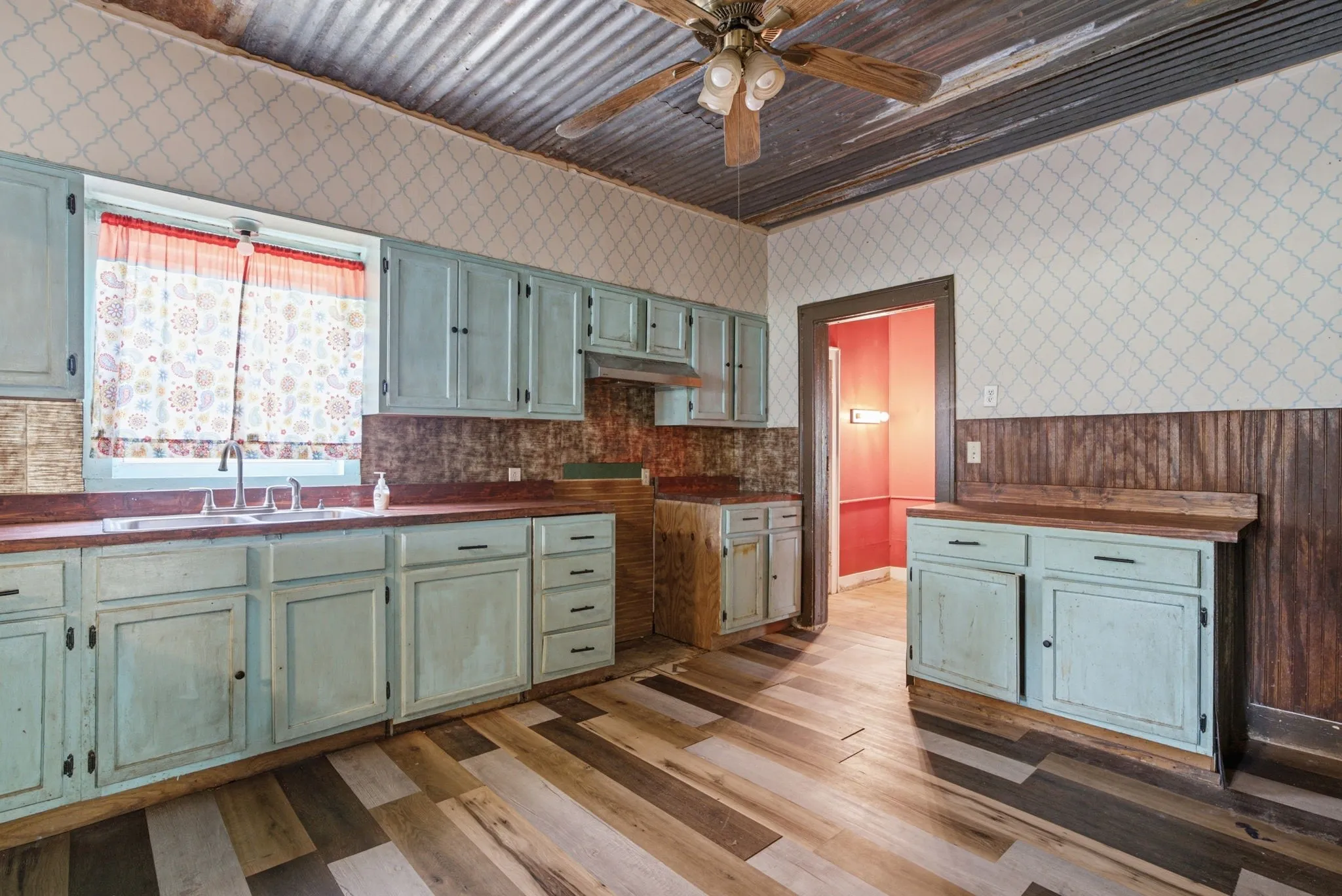 Kitchen with corrugated metal ceiling, patterned wallpaper, wood-finish flooring, and light blue cabinetry