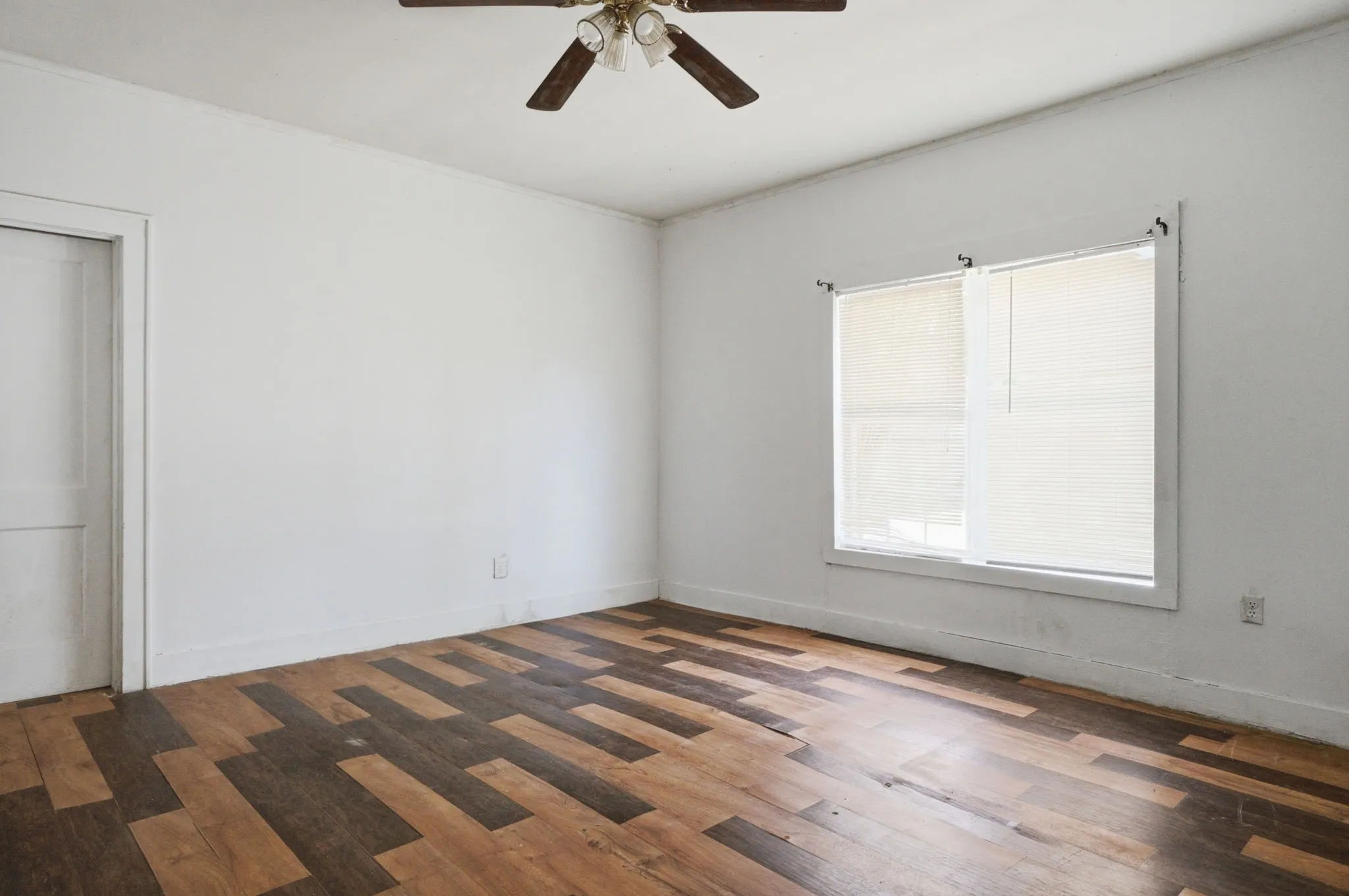 Room featuring multi-tone wood-finish flooring, white walls, and a ceiling fan with light fixture