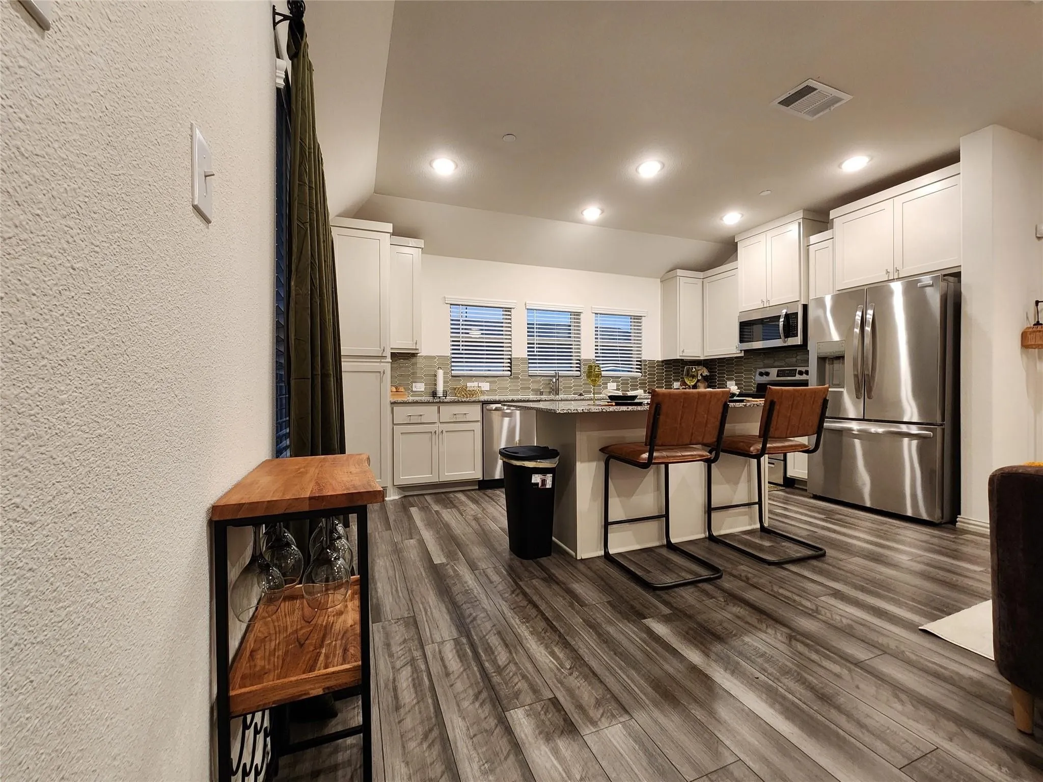 Kitchen featuring stainless steel appliances, upper and lower cabinetry, an island with countertop seating, and wood-finish flooring