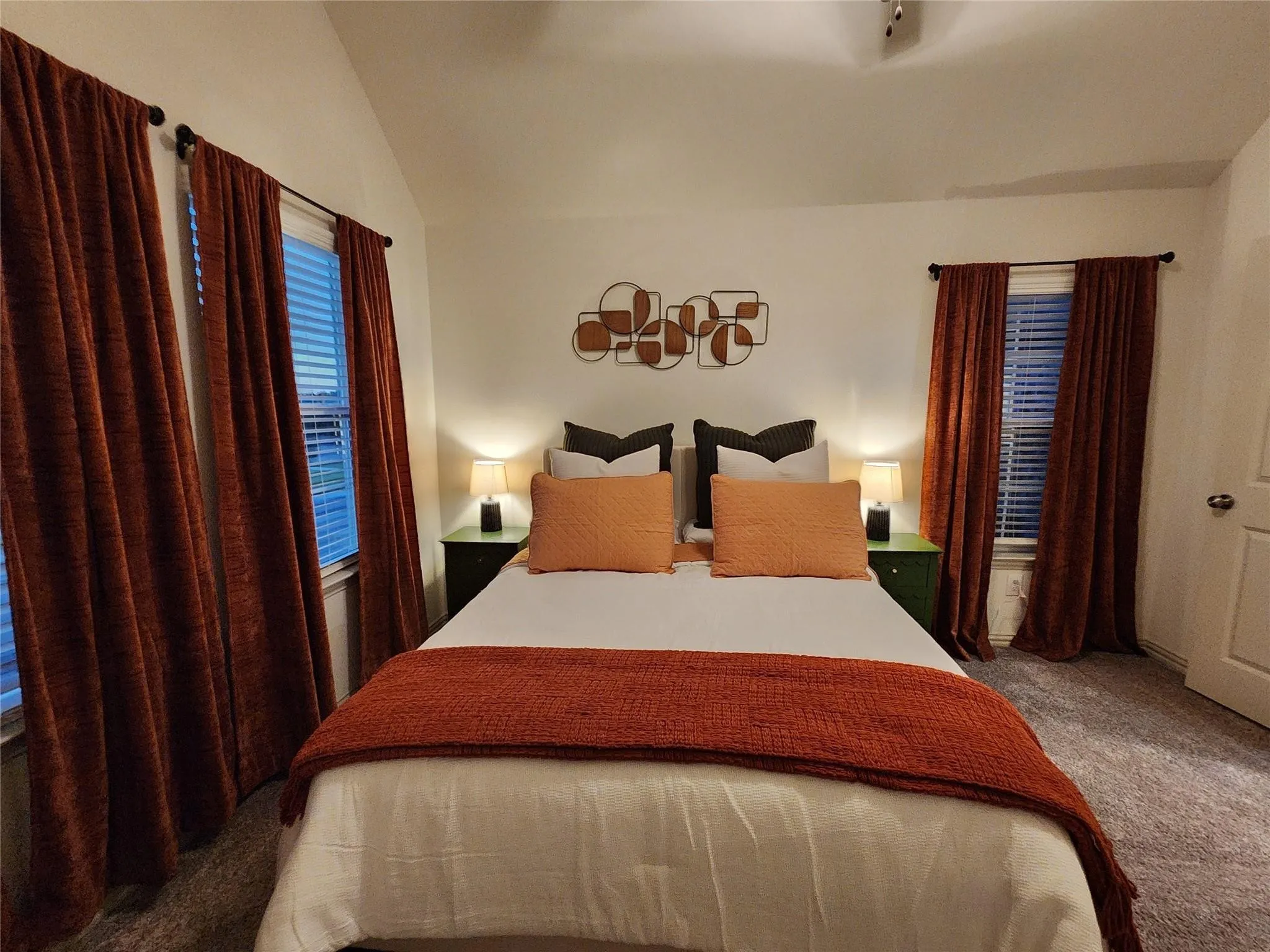 Vaulted ceiling with track lighting, dual windows with blinds, and wall-to-wall carpeting