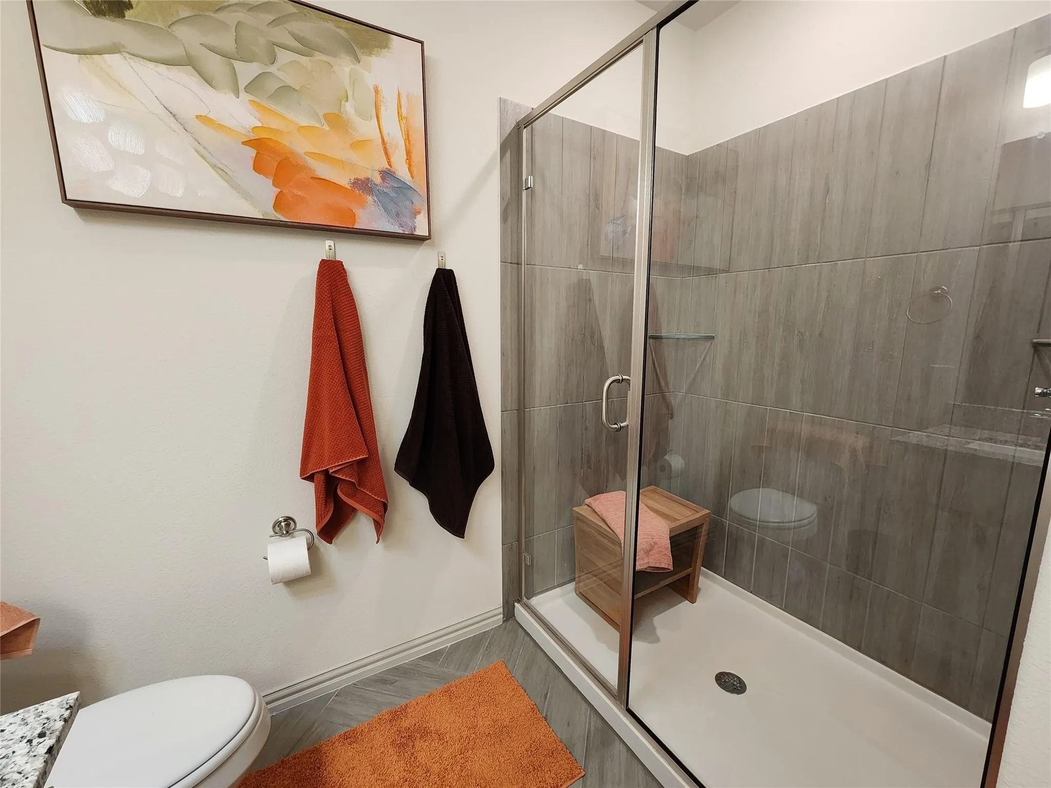 Walk-in shower with clear glass enclosure, gray wood-finish tile surround, and a built-in shelf