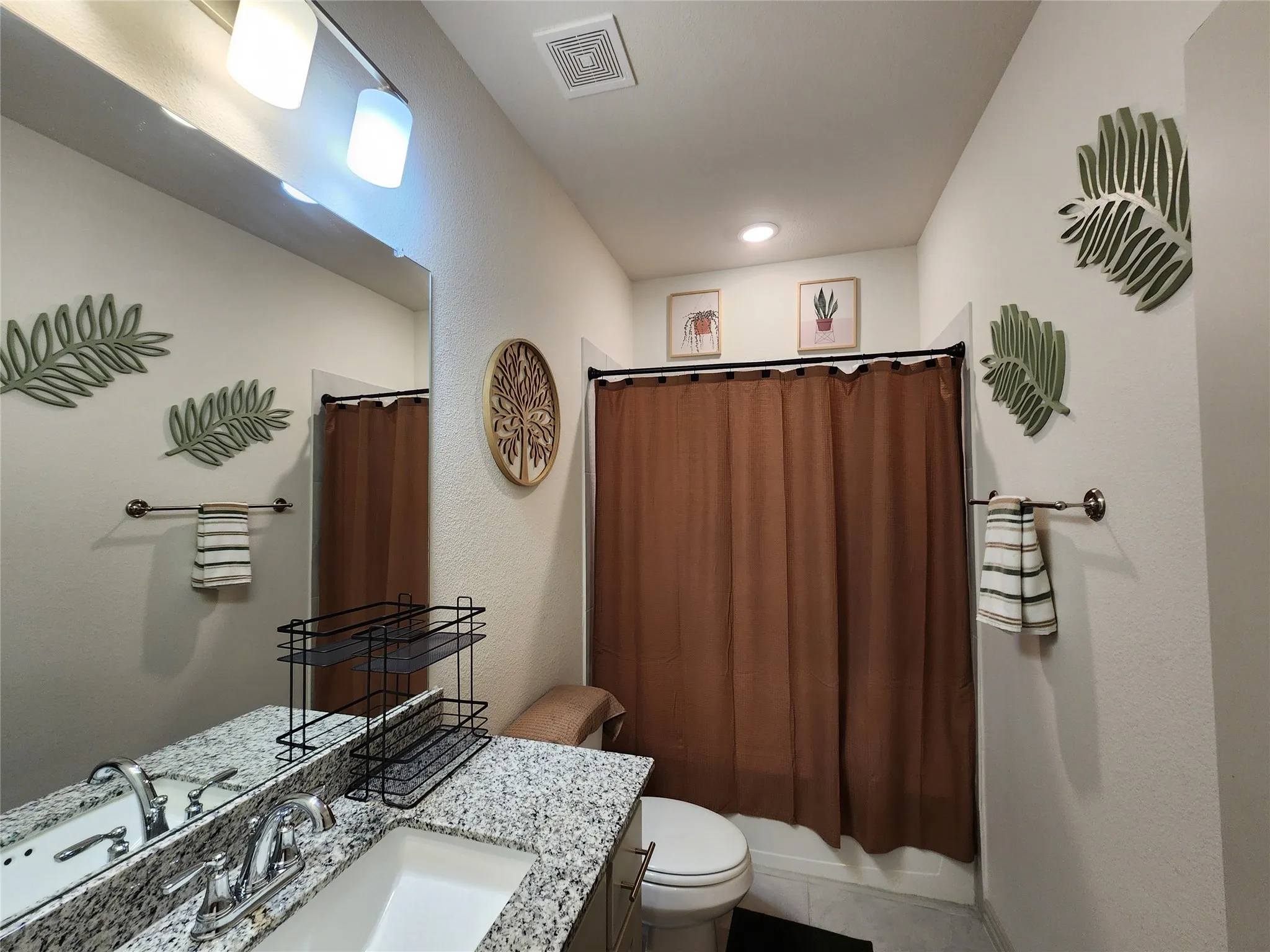 Bathroom featuring a granite-finish countertop, single basin sink, chrome faucet, wall-mounted mirror, and overhead track lighting