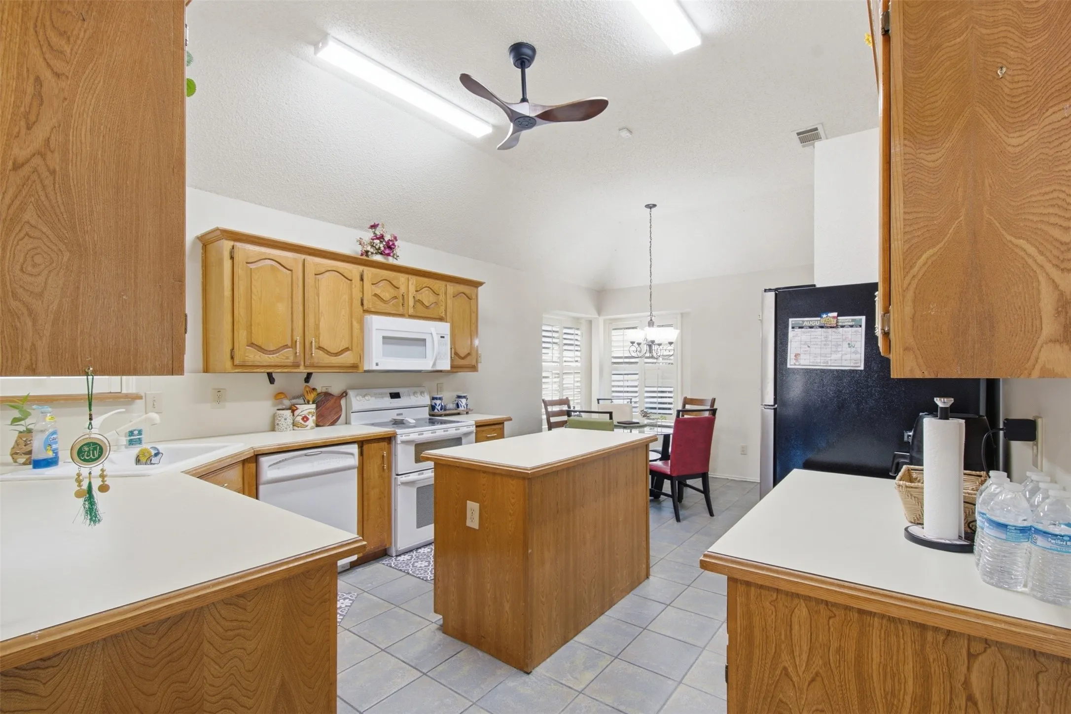 Kitchen featuring wood-finish cabinetry, white countertops, a central island, and white appliances