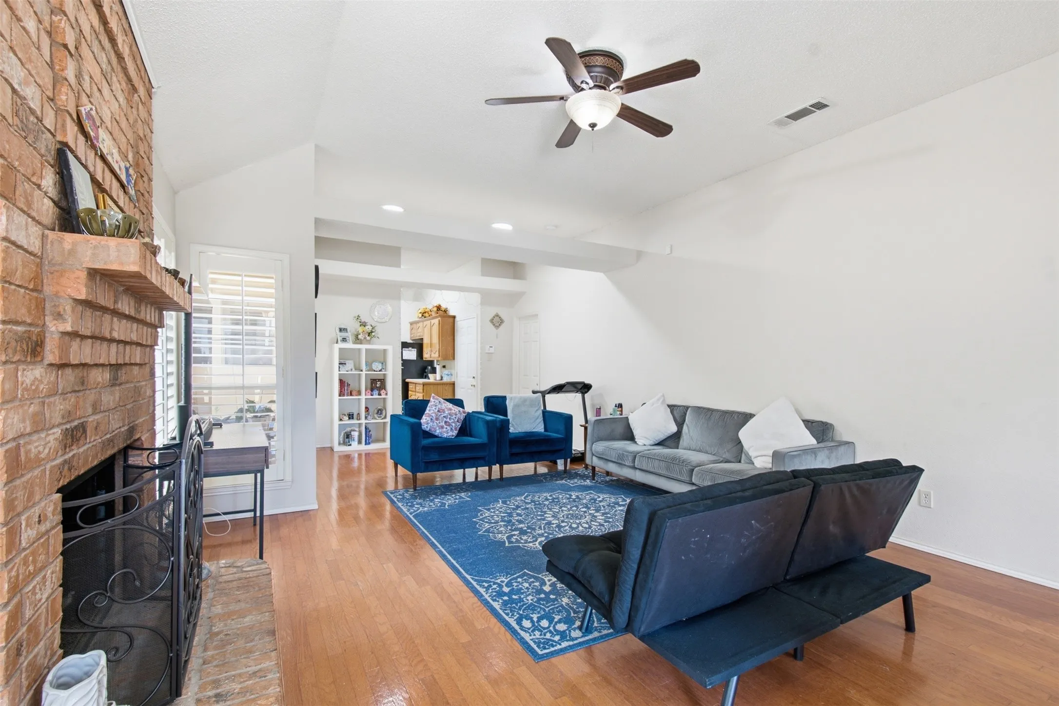 Brick-faced fireplace with a wooden mantel, wood-finish flooring, vaulted ceilings, and a ceiling fan